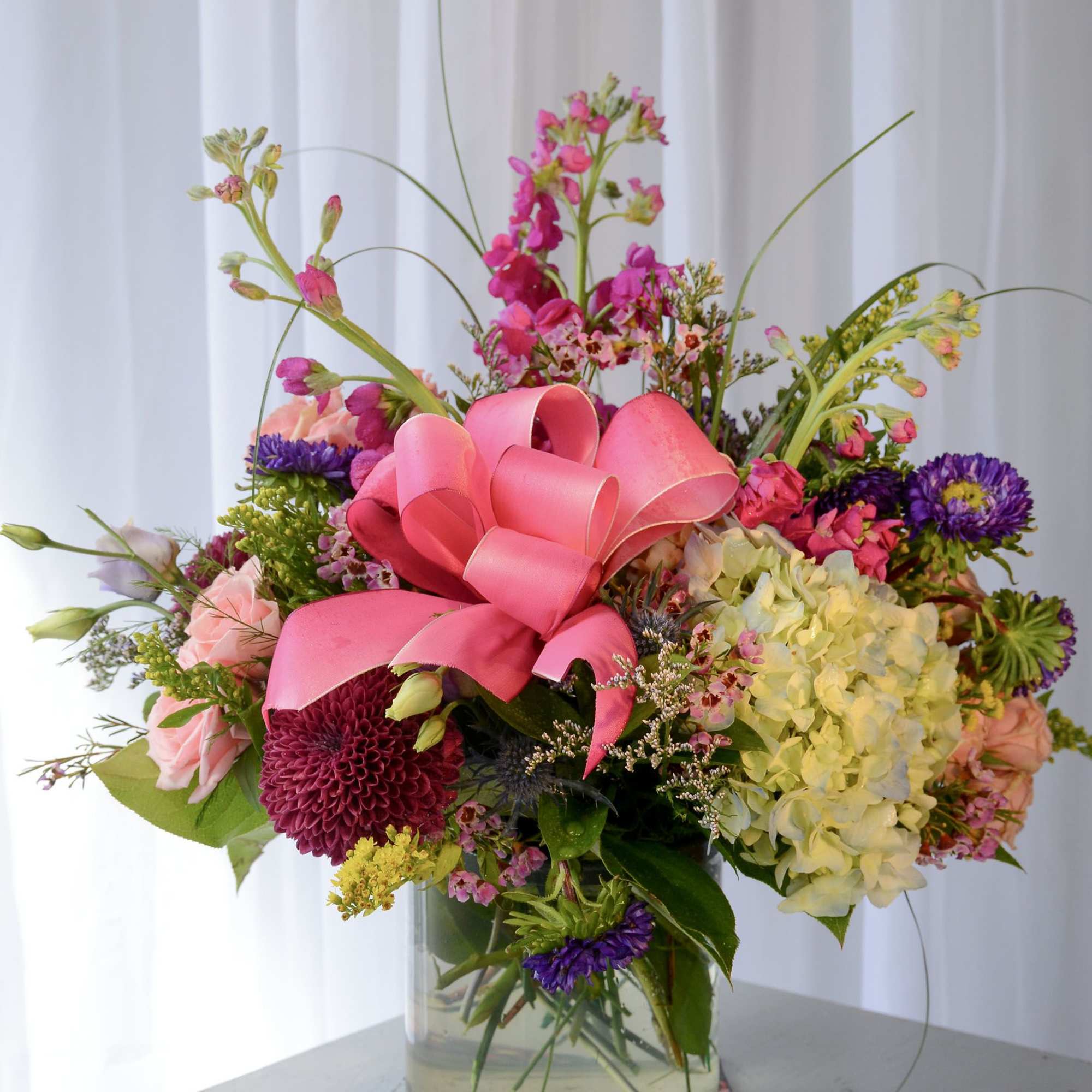 Colorful mixed bouquet in a clear glass vase with a pink ribbon bow