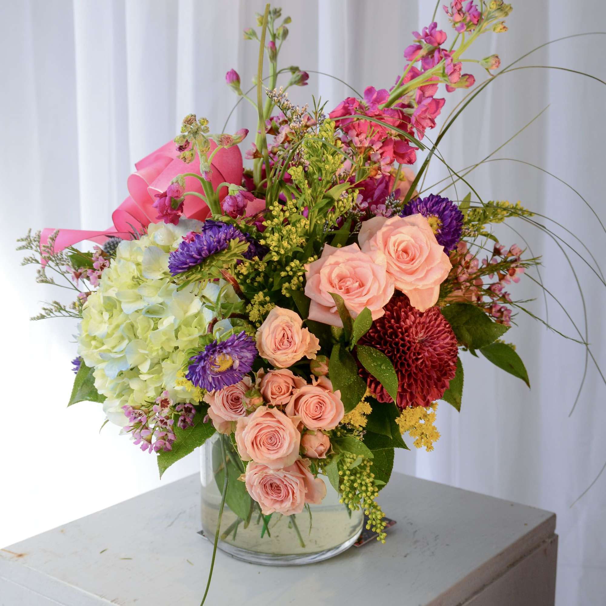 Mixed bouquet in a clear glass vase with pink, peach, purple, and green blooms