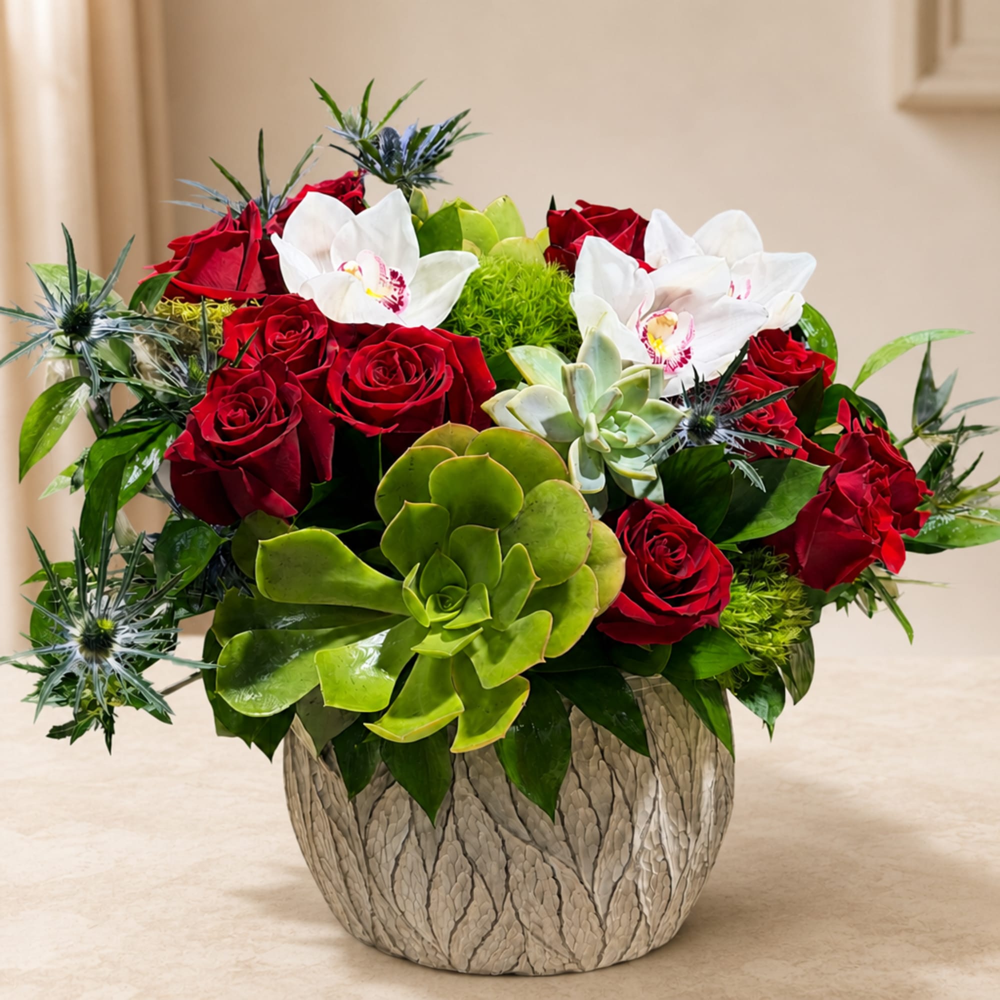 Red roses and white orchids arranged with succulents in a textured vase