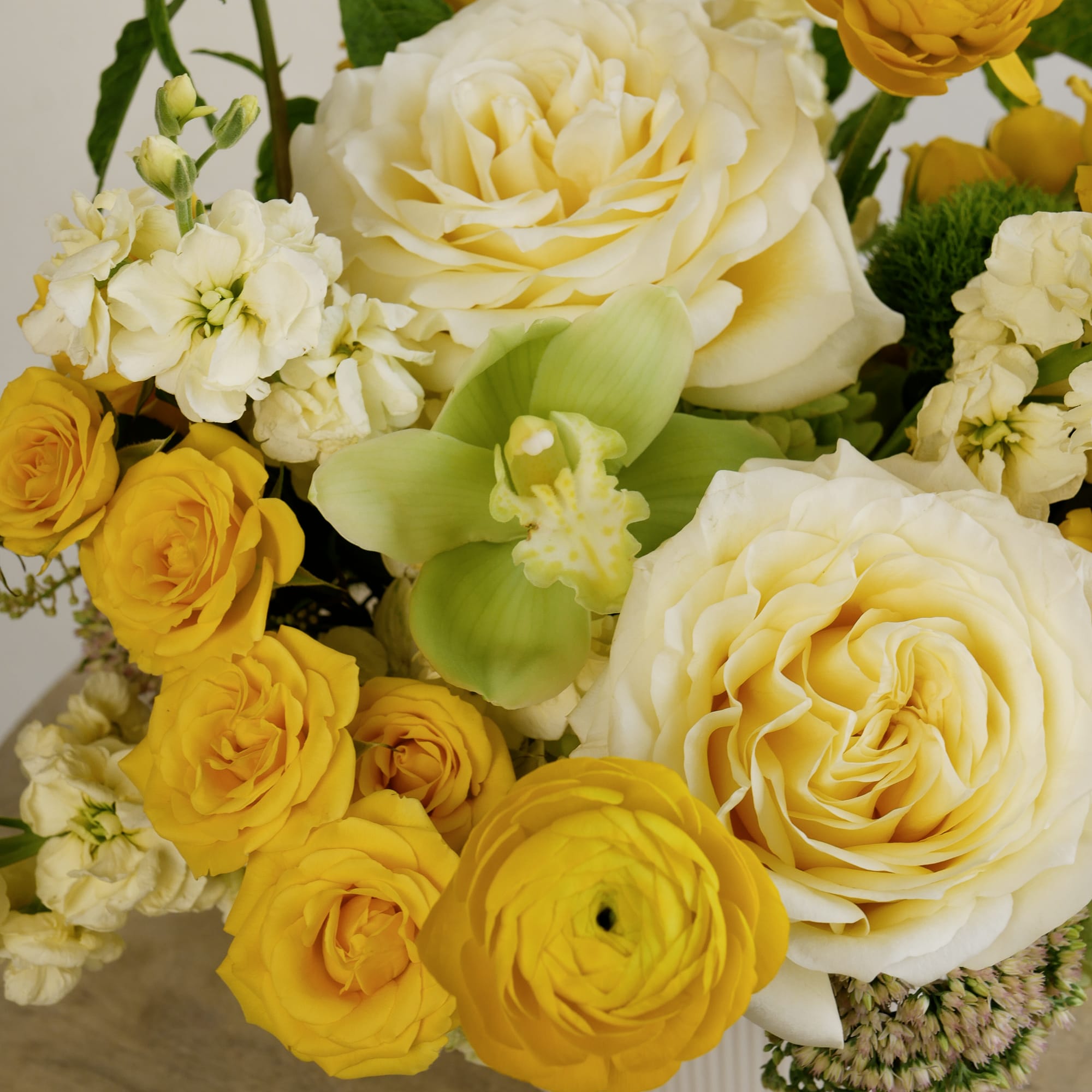 Bouquet of cream and yellow roses with white blossoms and green orchid accents