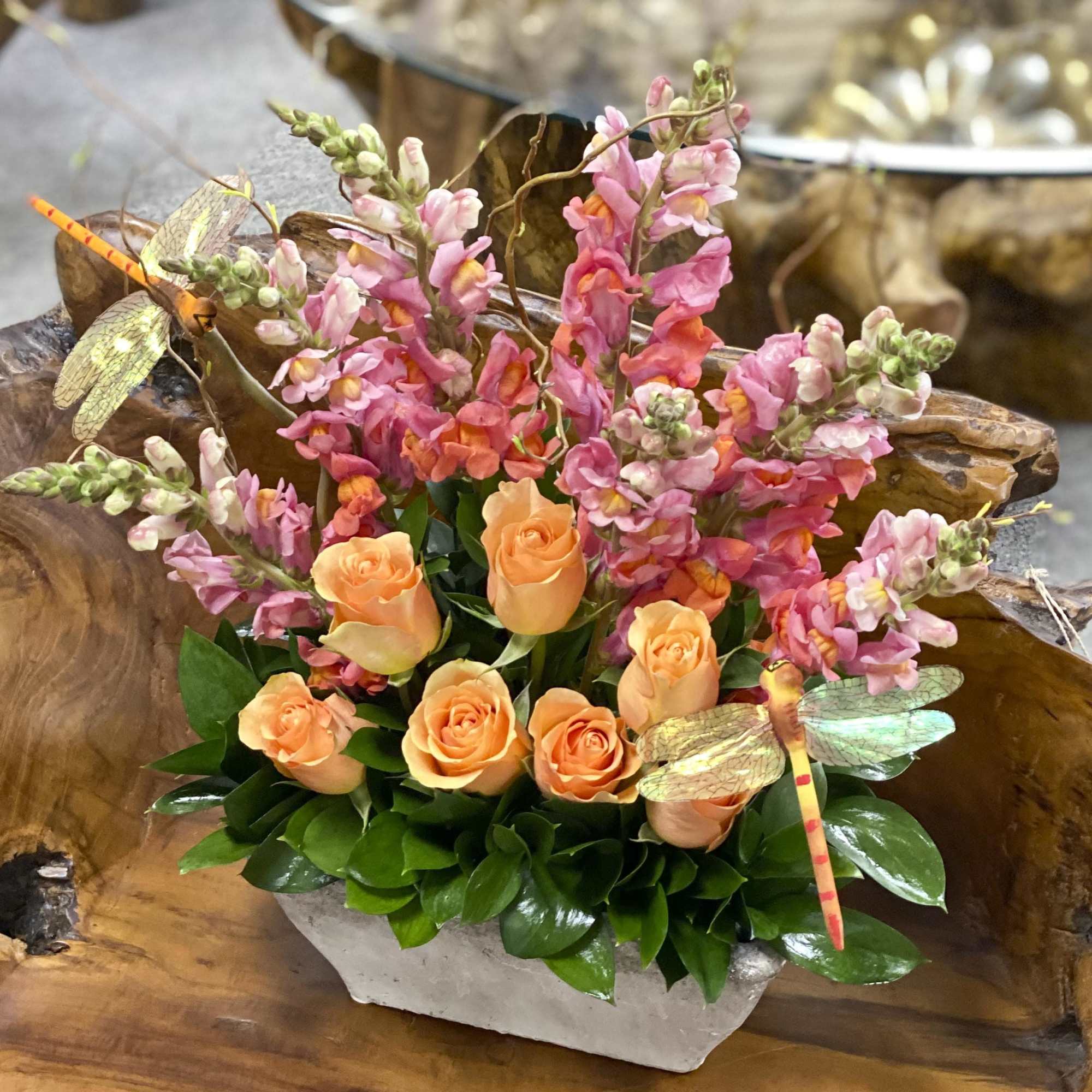 Orange roses with pink snapdragons and dragonfly picks in a low container