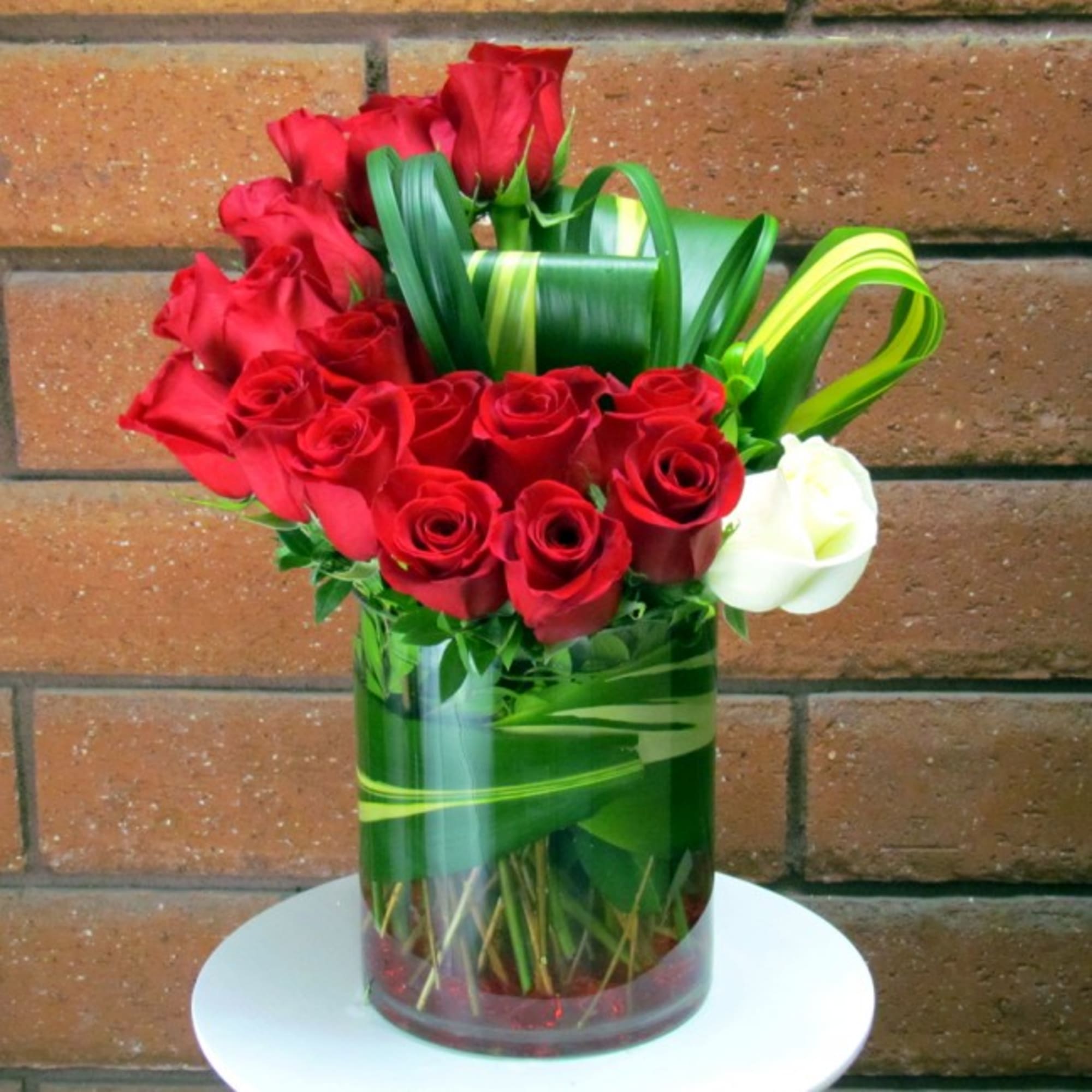 Red roses arranged in a glass vase with green ribbon accents