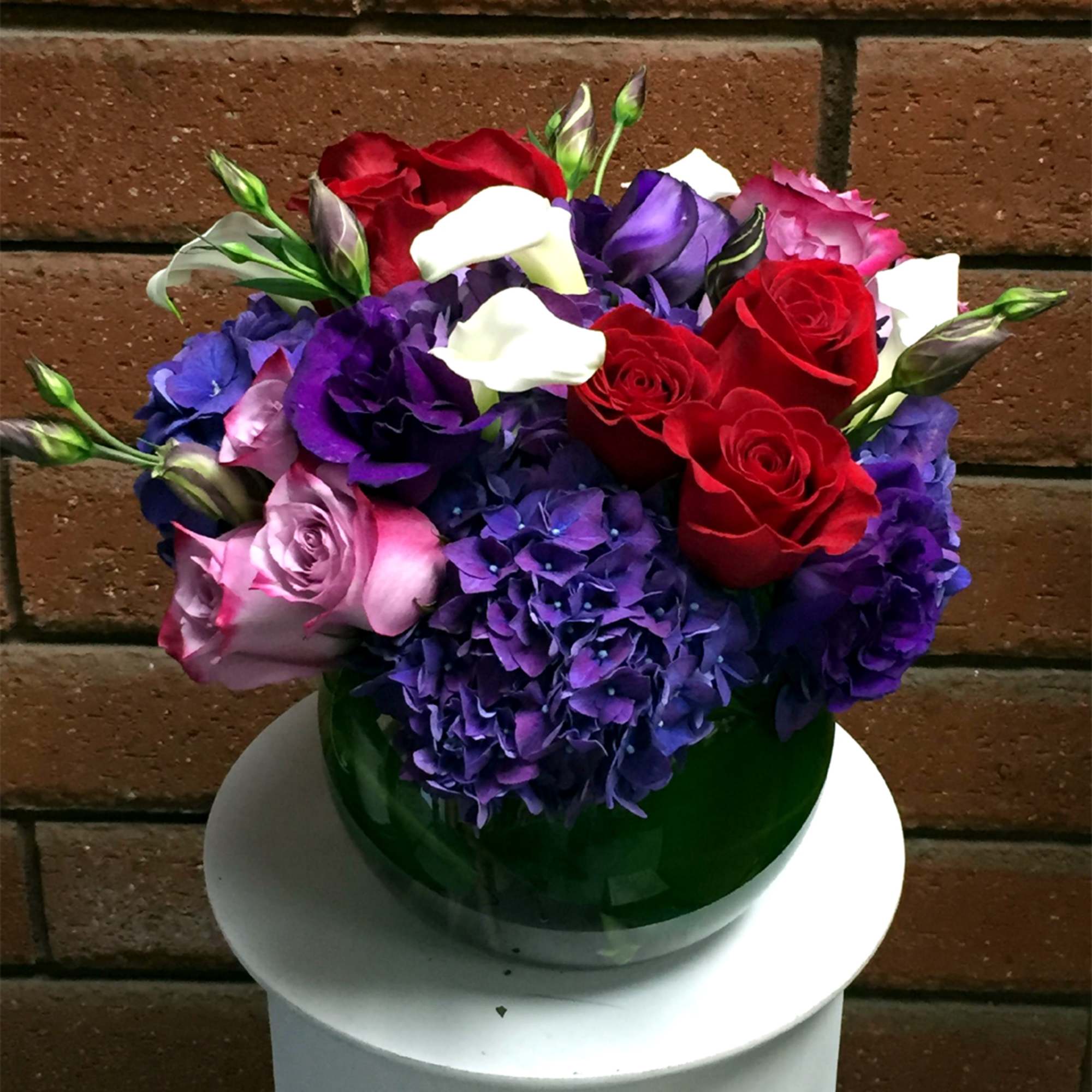 Bouquet of red roses, purple hydrangeas, and white calla lilies in a green vase