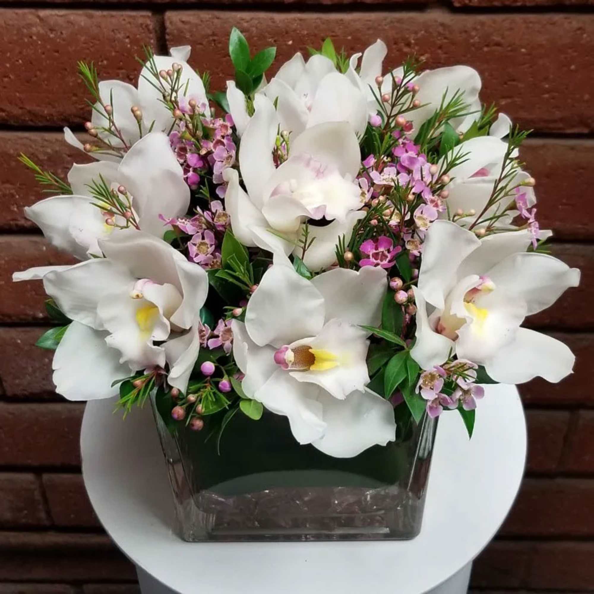 White orchid arrangement in a square glass vase with pink filler flowers