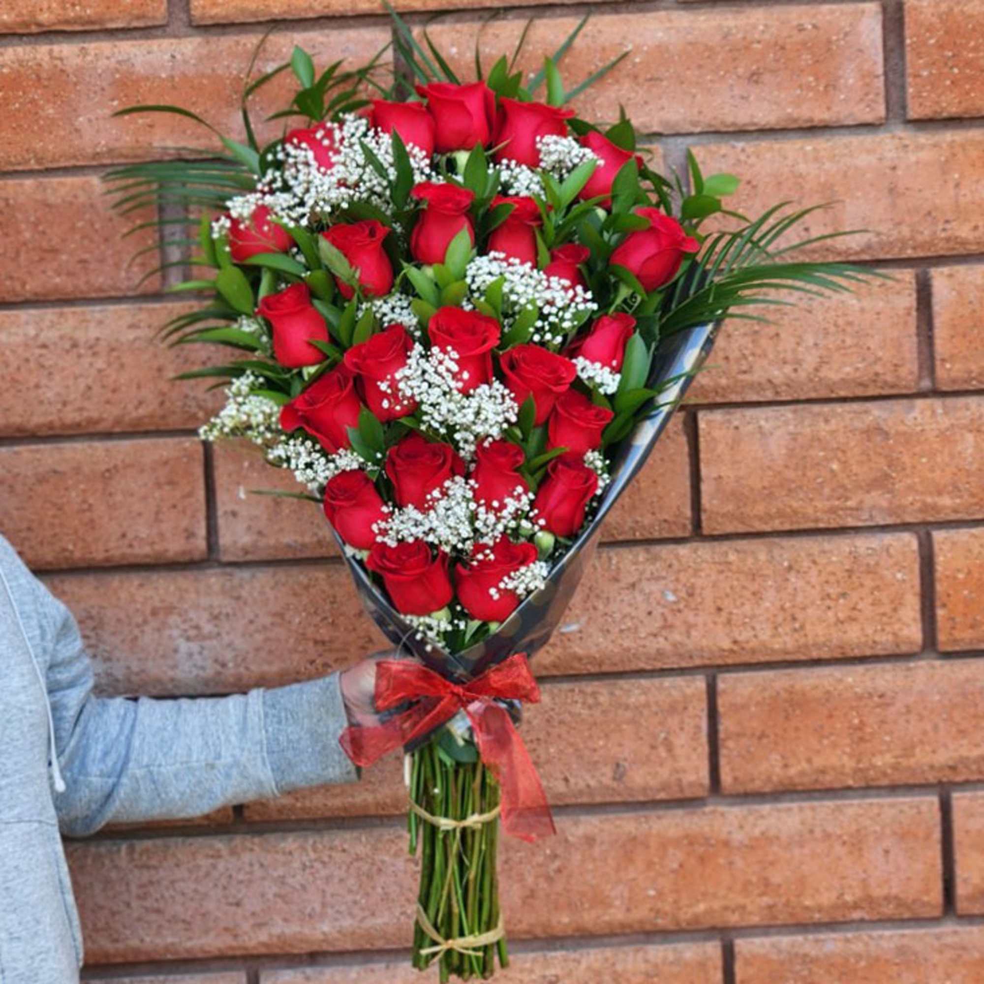 Bouquet of red roses with baby's breath wrapped in dark paper and tied with a red ribbon
