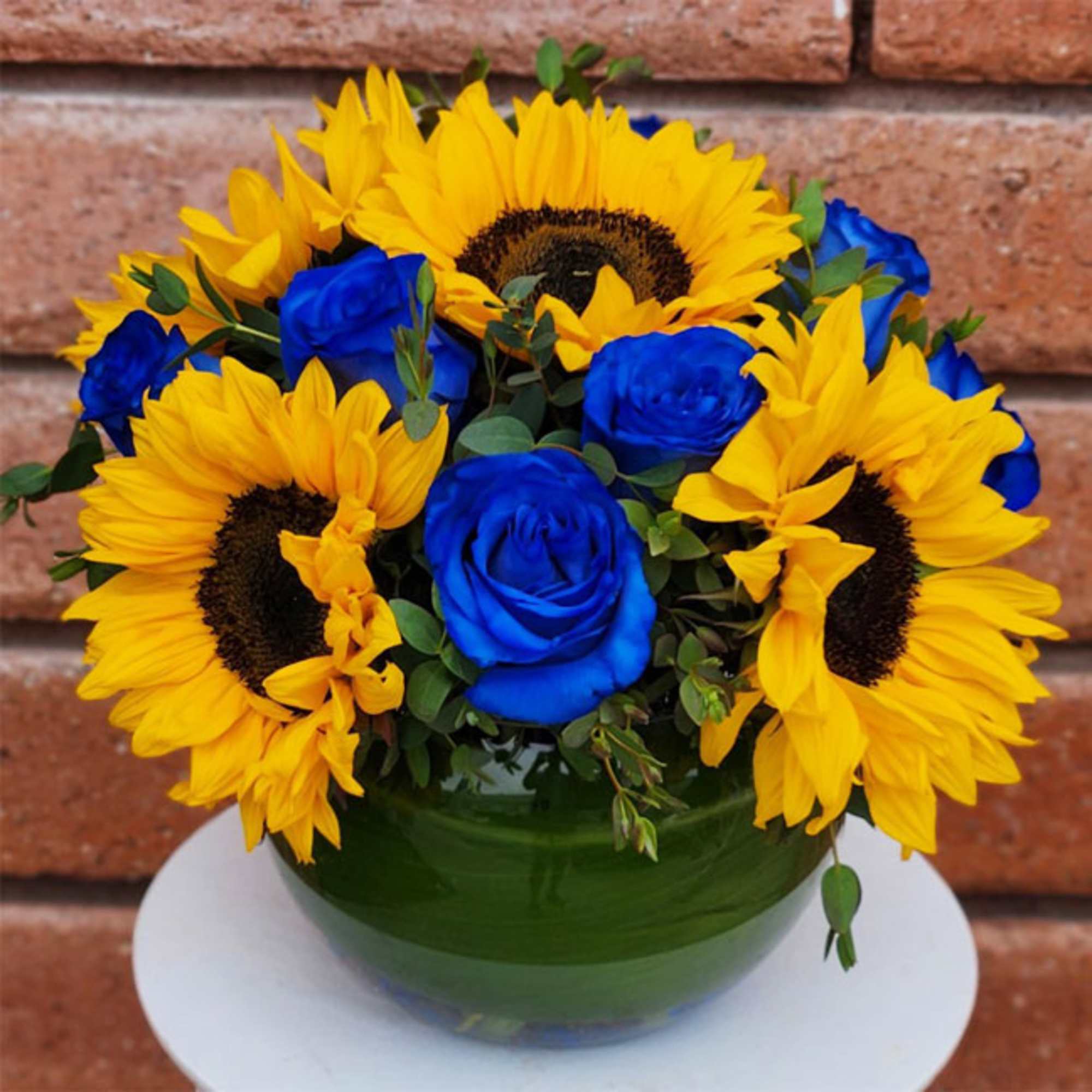 Bouquet of yellow sunflowers and blue roses in a green glass vase
