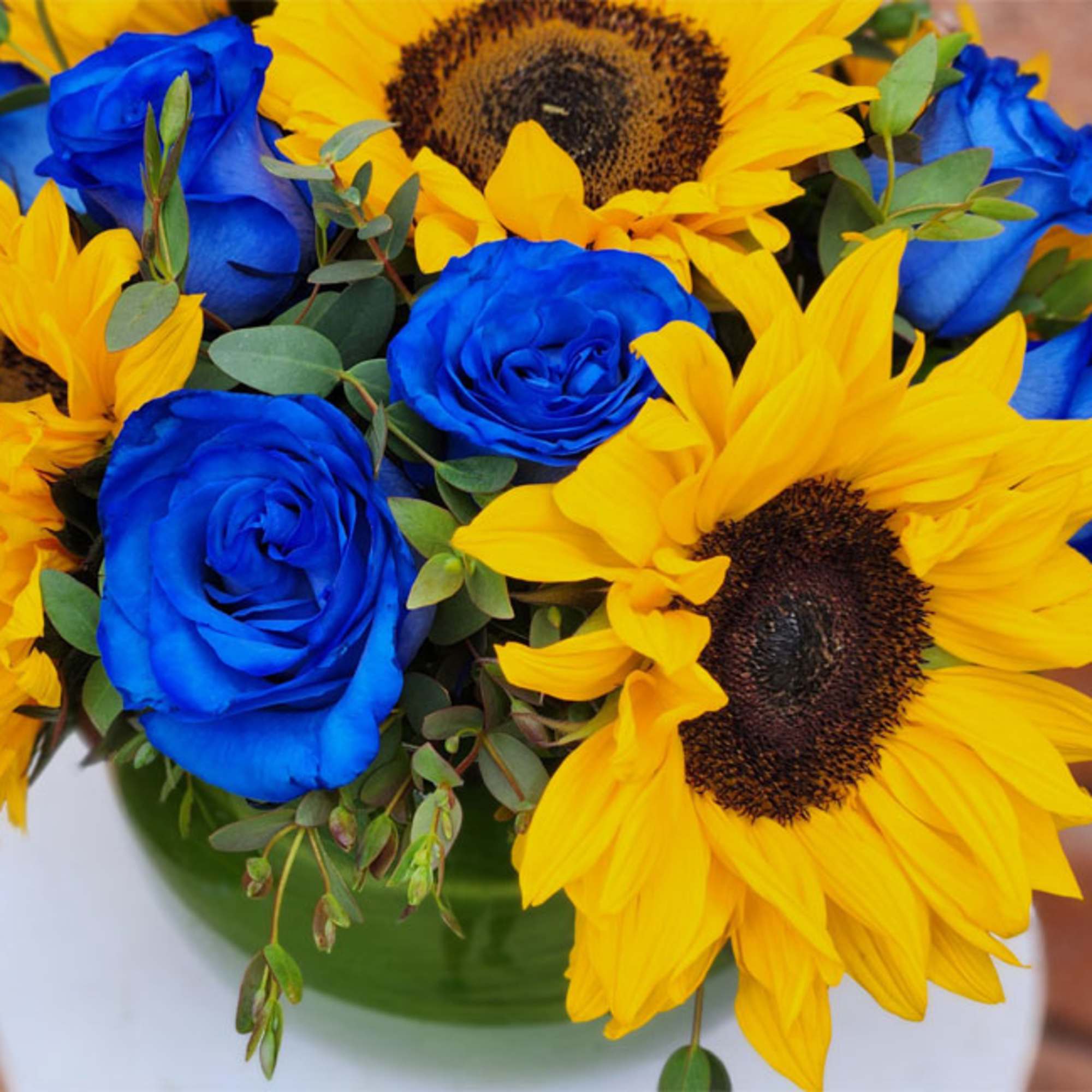 Blue roses and yellow sunflowers in a green vase