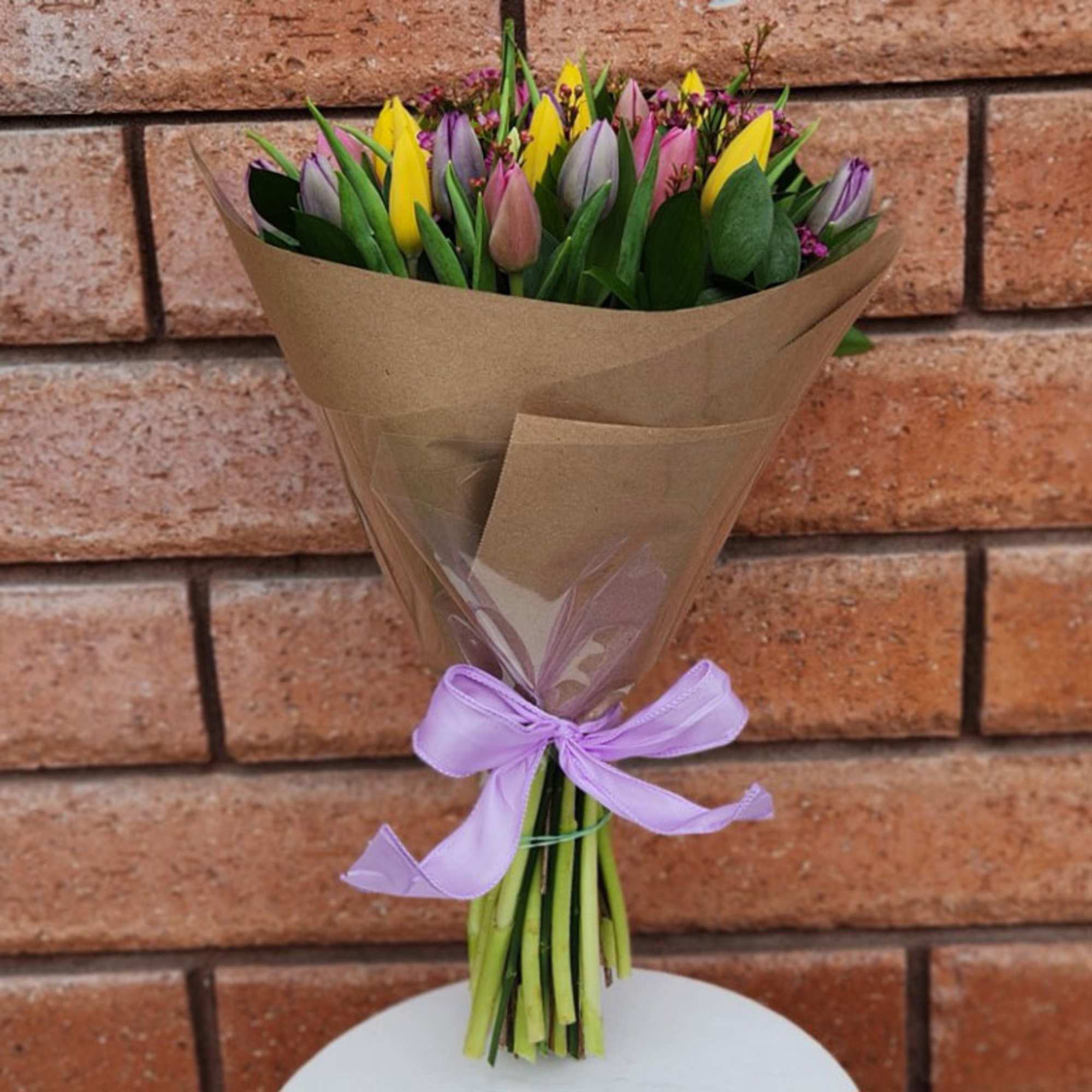 Bouquet of multicolored tulips wrapped in brown paper with a purple ribbon
