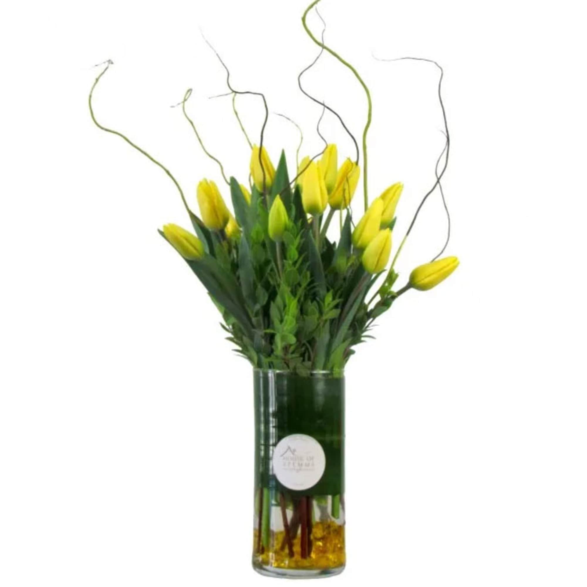 Yellow tulips arranged in a tall glass vase with curly branches