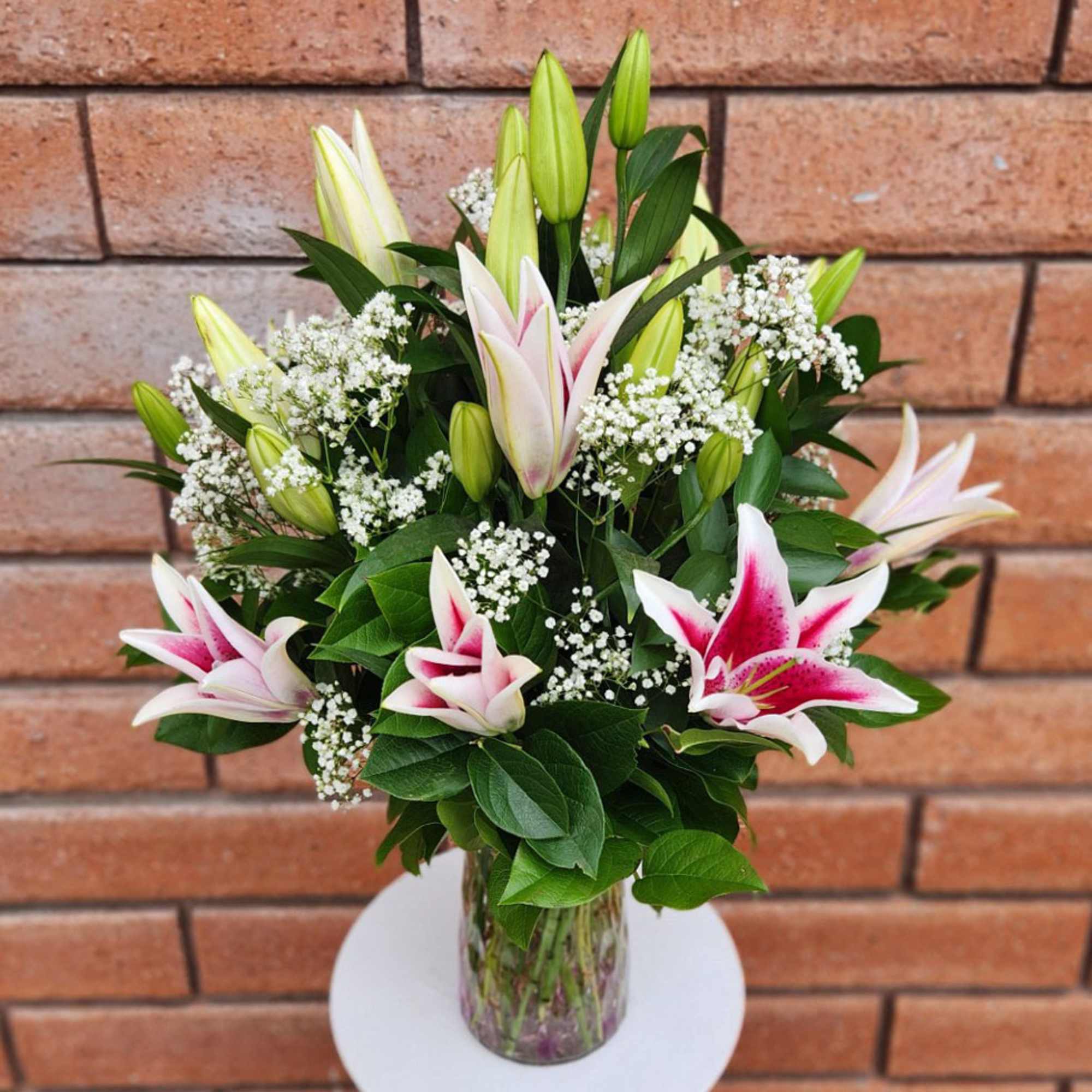 Tall glass vase of pink and white lilies with baby's breath in a lush upright bouquet