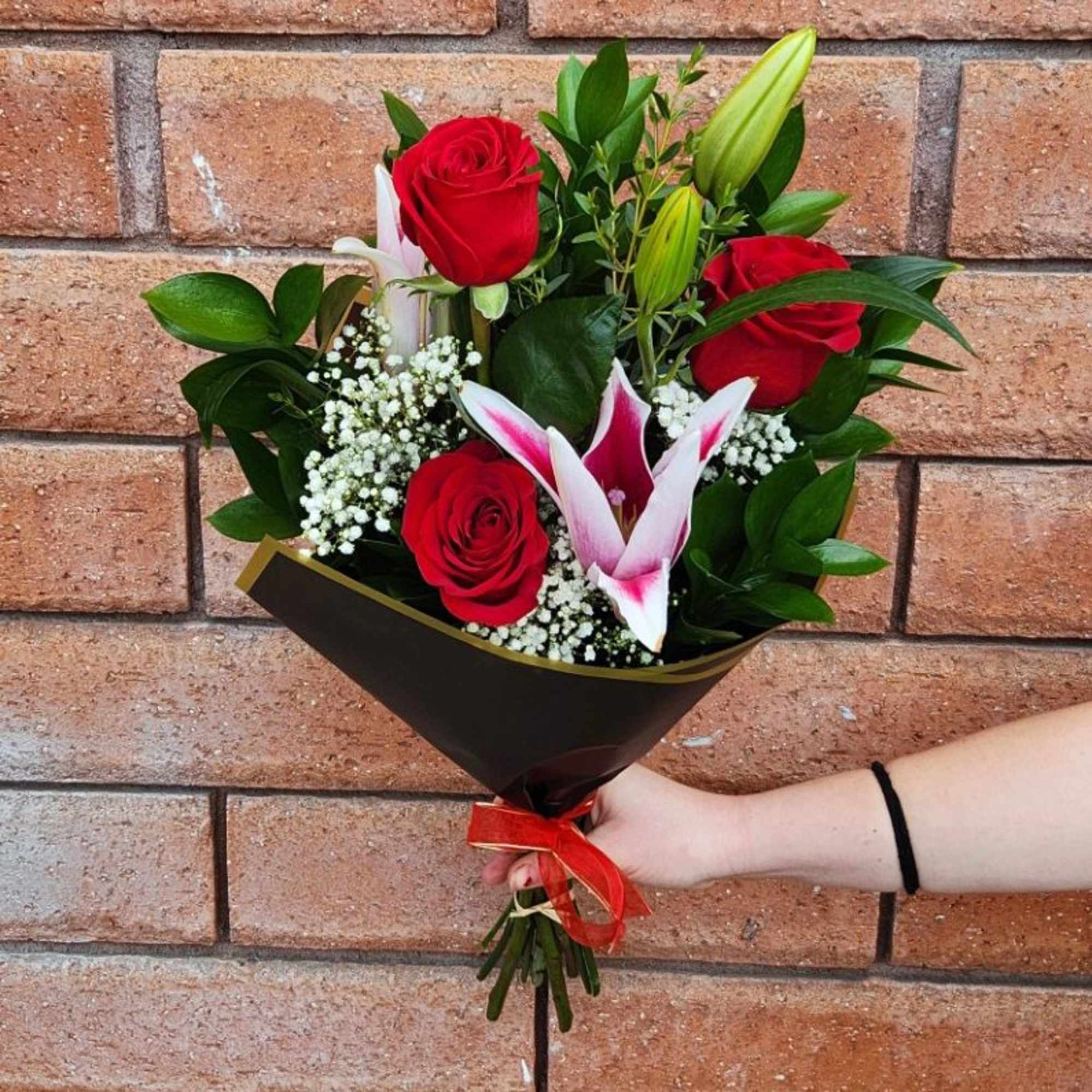 Bouquet of red roses and white lilies wrapped in dark paper