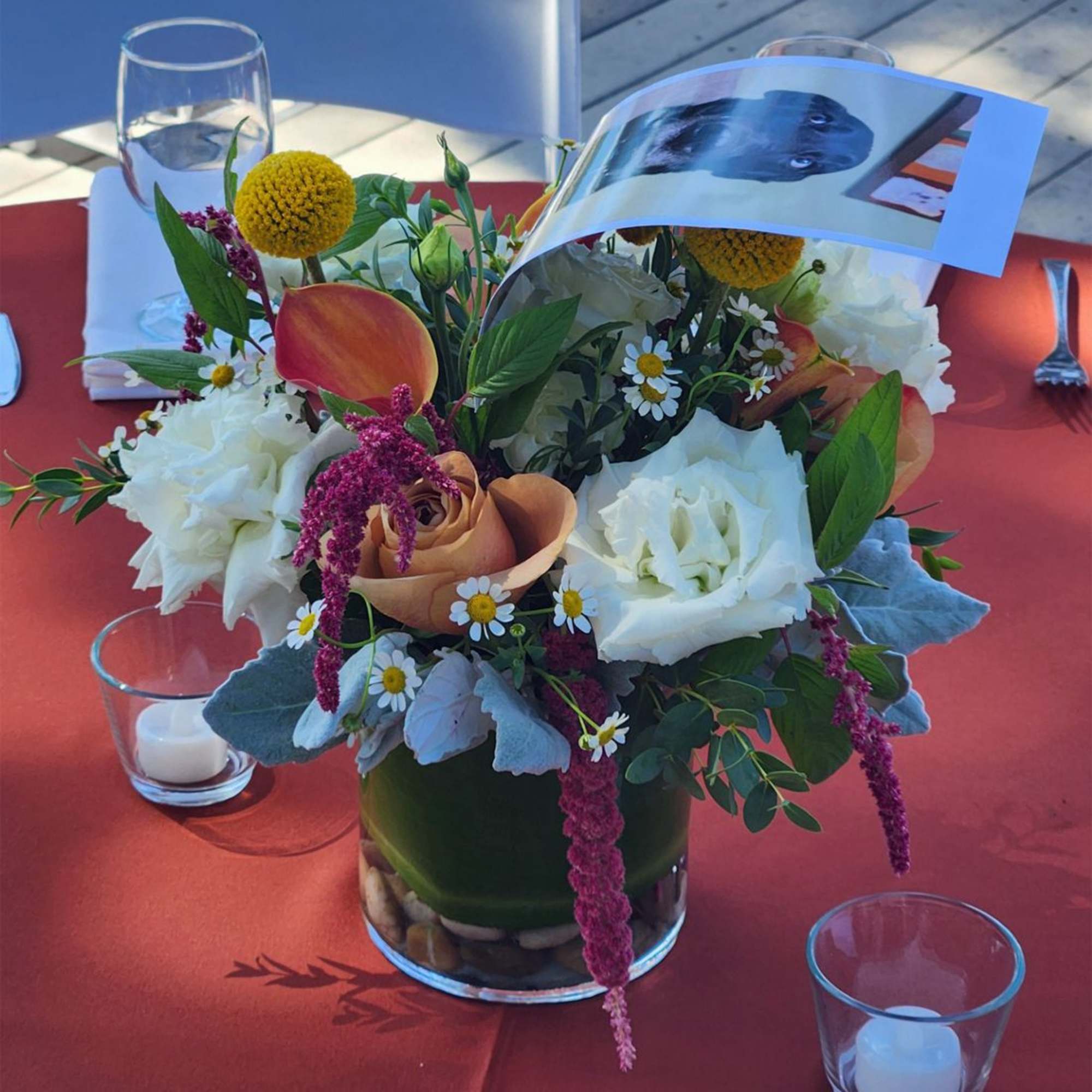 Mixed floral centerpiece in a glass vase with a photo card tucked in