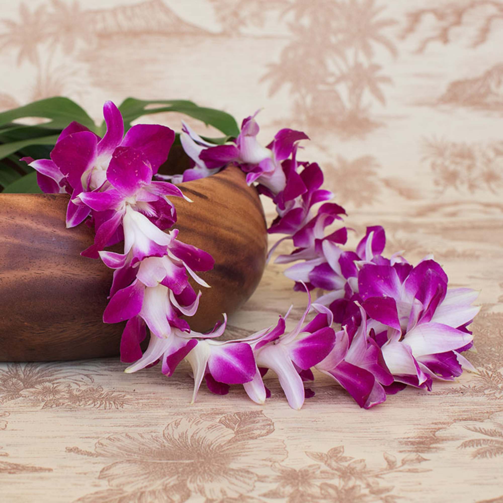 Purple and white orchid lei draped over a wooden bowl on a patterned surface