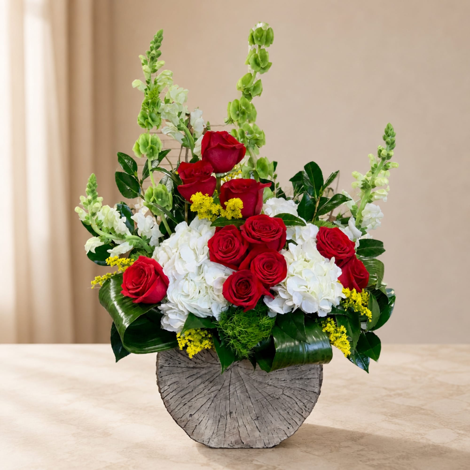 Red roses and white hydrangeas arranged in a gray vase with tall green spikes