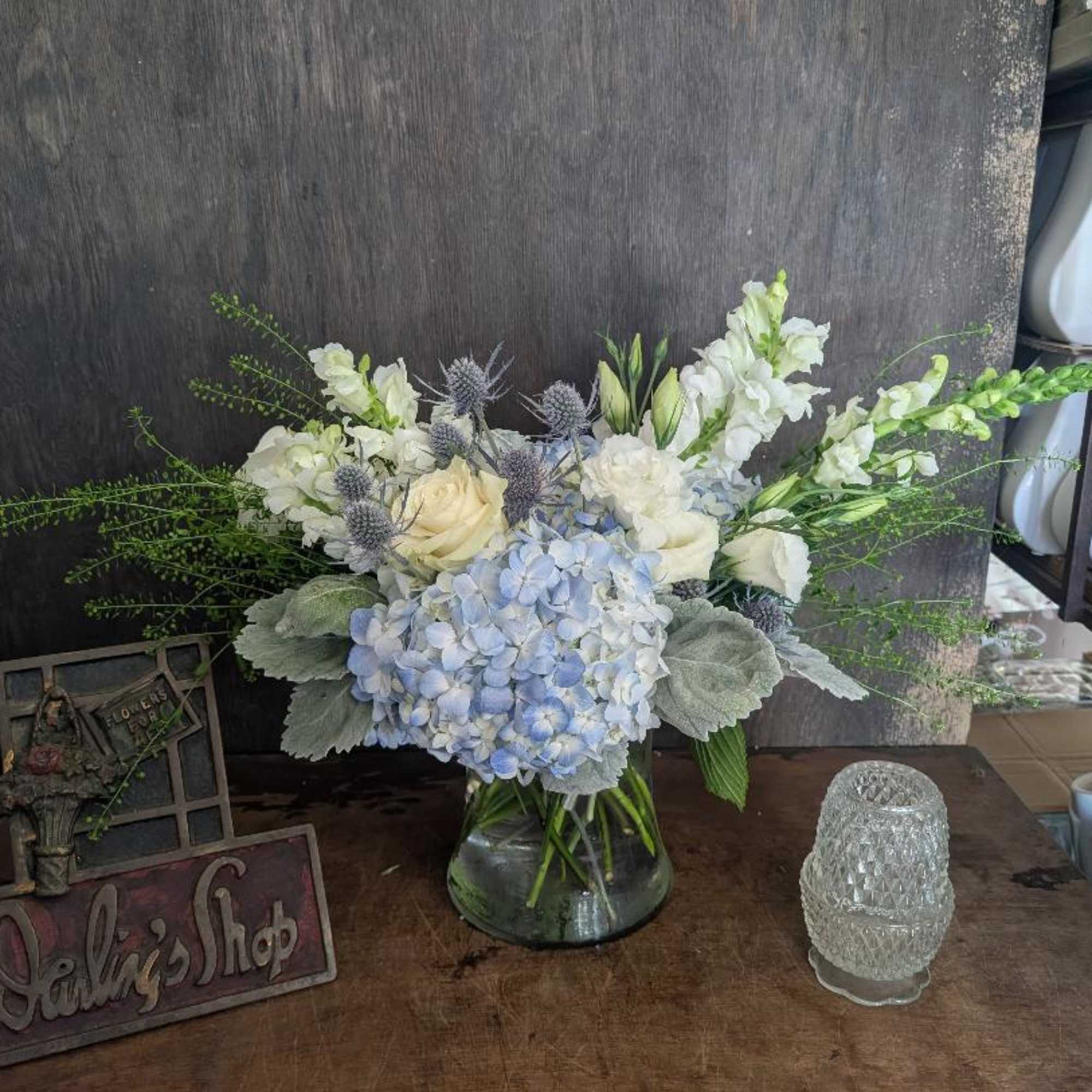 Blue hydrangeas and white flowers arranged in a glass vase