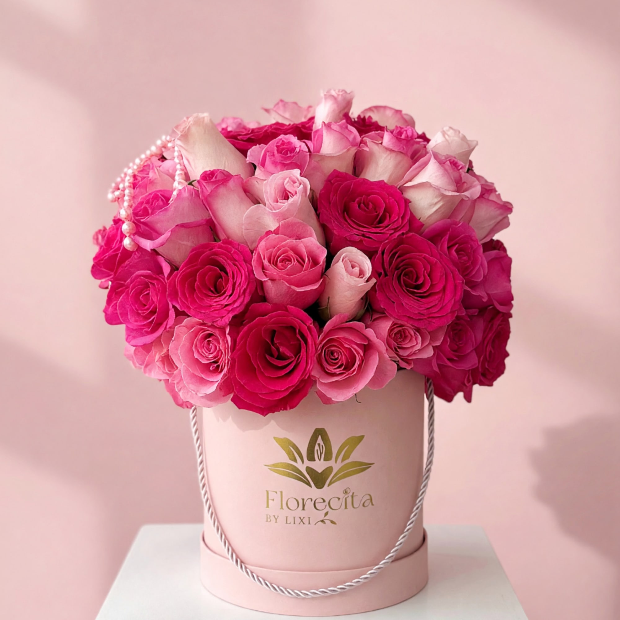 Pink and white roses arranged in a round hatbox with a pearl strand