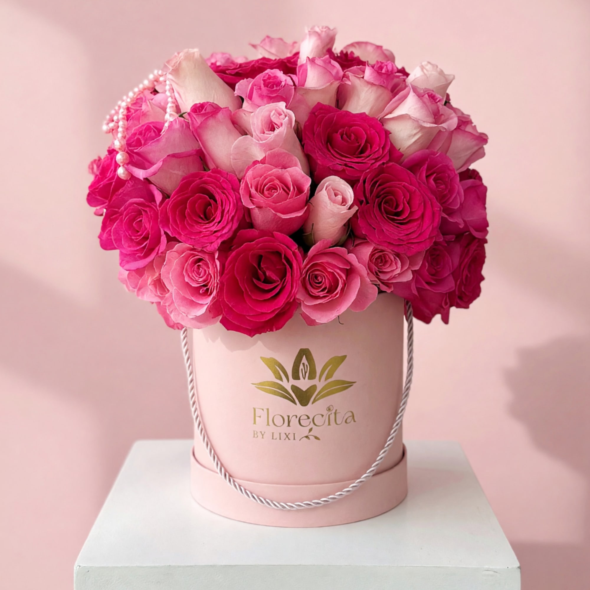 Pink and white roses arranged in a round hatbox with a pearl strand