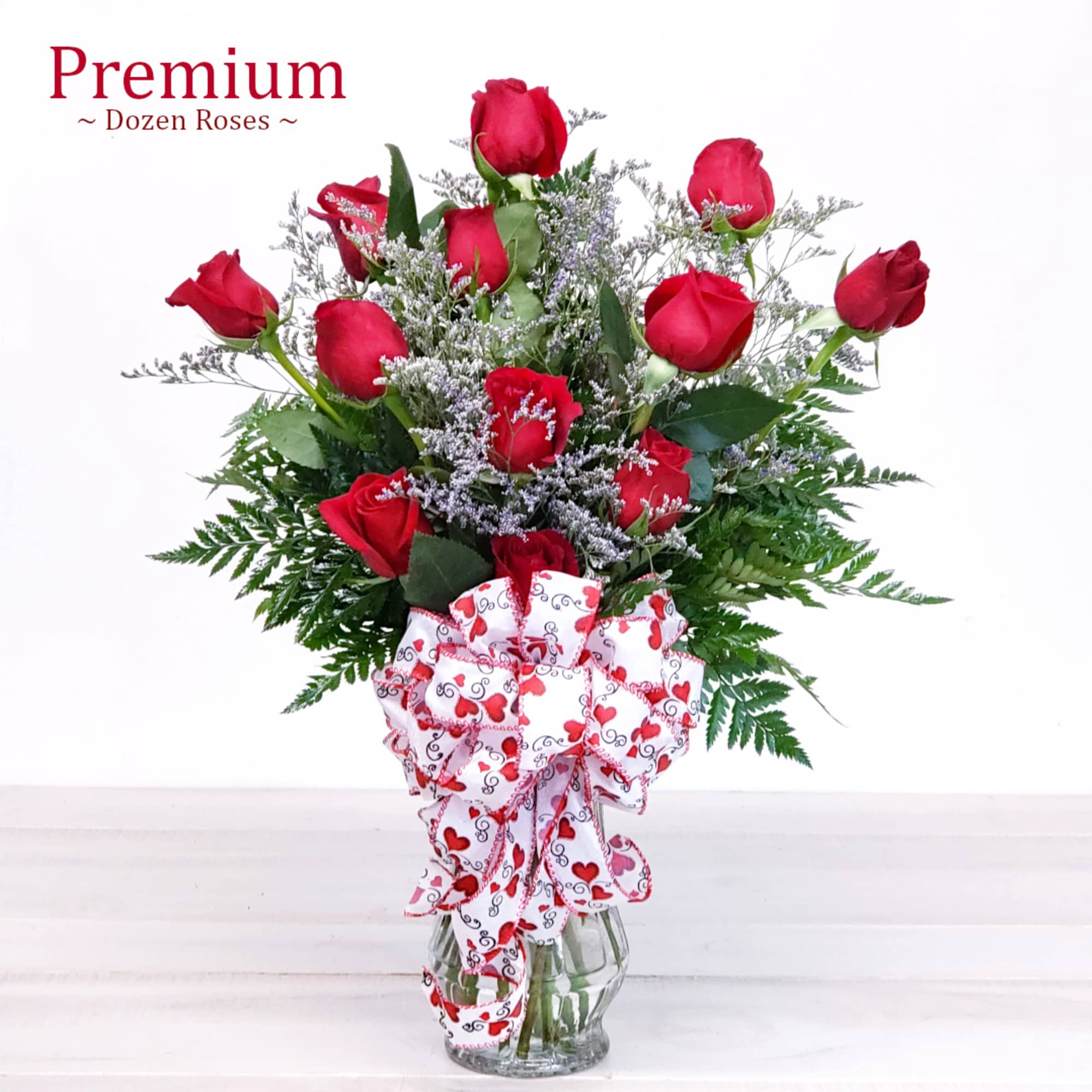 Dozen red roses in a clear glass vase with a heart-patterned bow