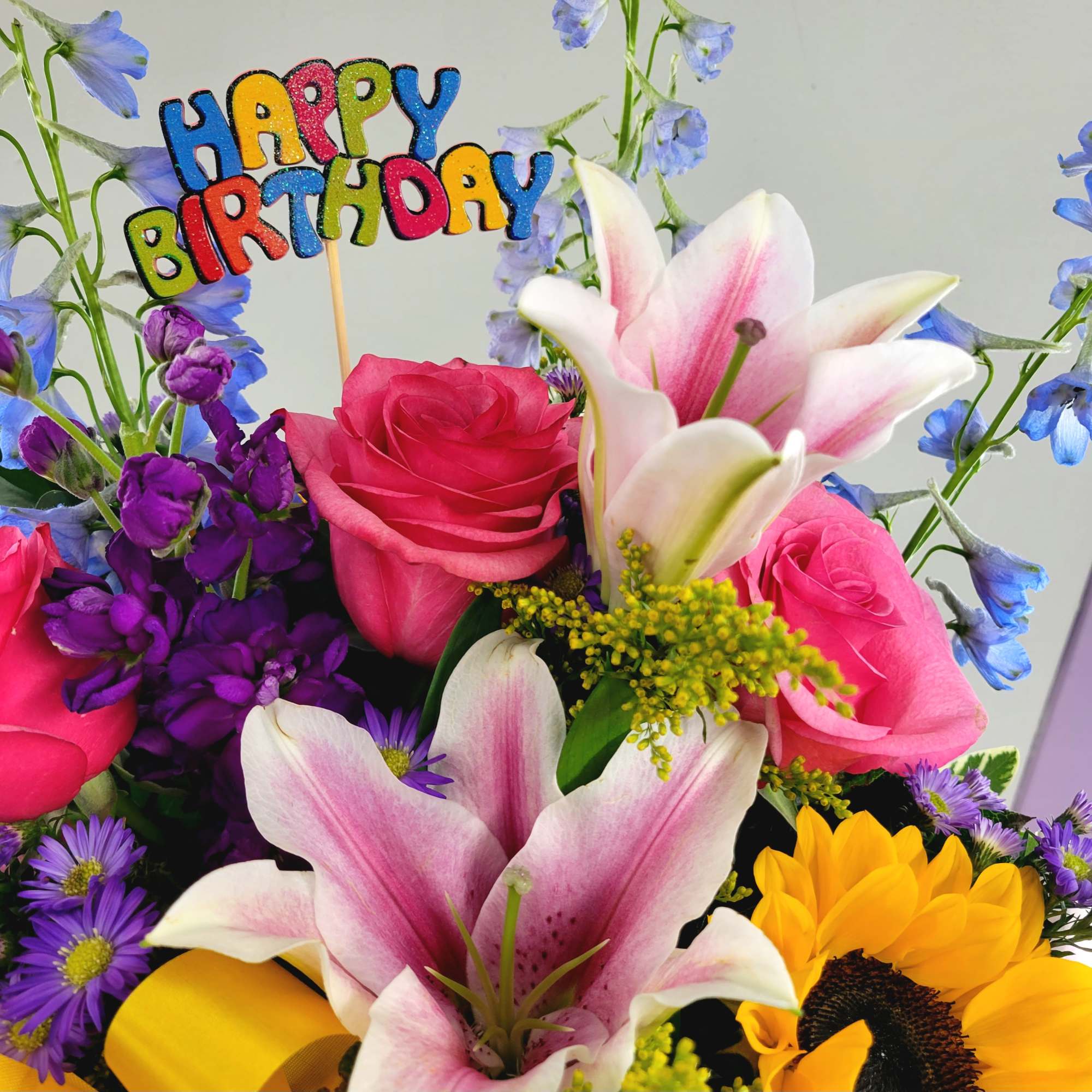 Colorful birthday bouquet with roses, lilies, and a sunflower topper