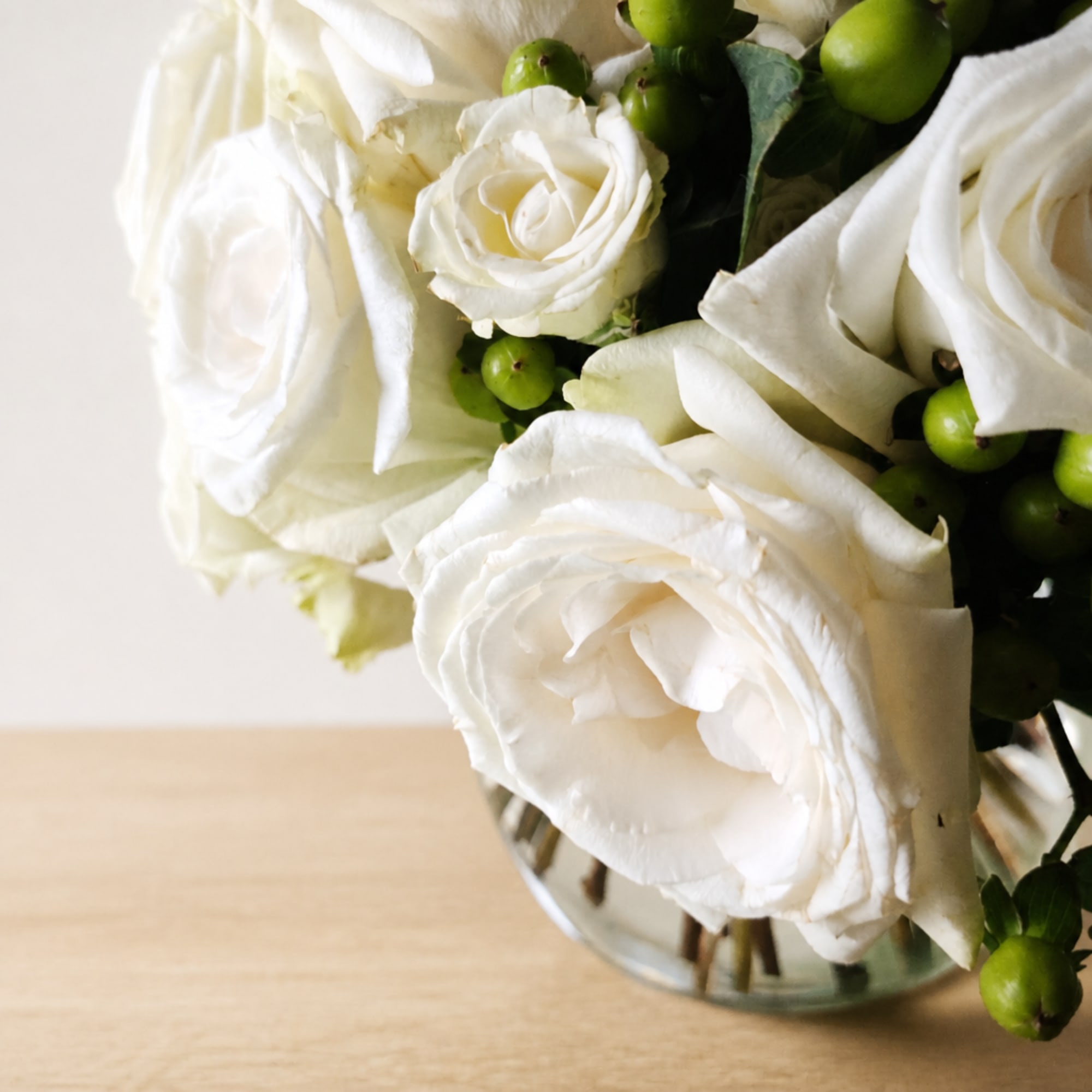 White roses arranged in a clear glass vase with green berries