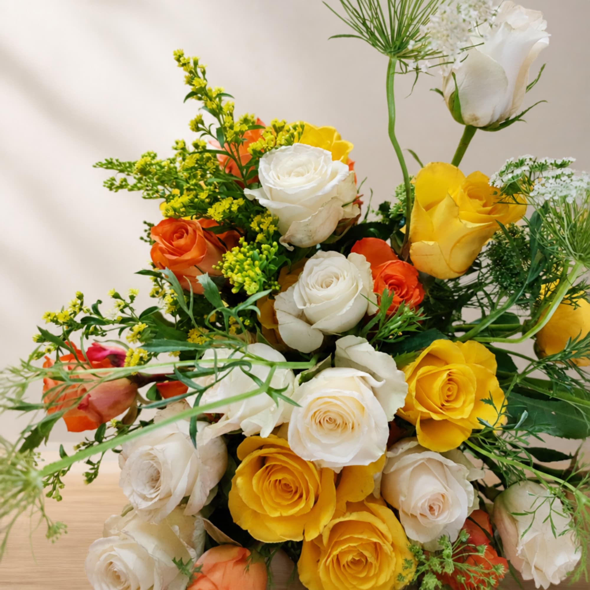 Bouquet of white, yellow, and orange roses with airy greenery