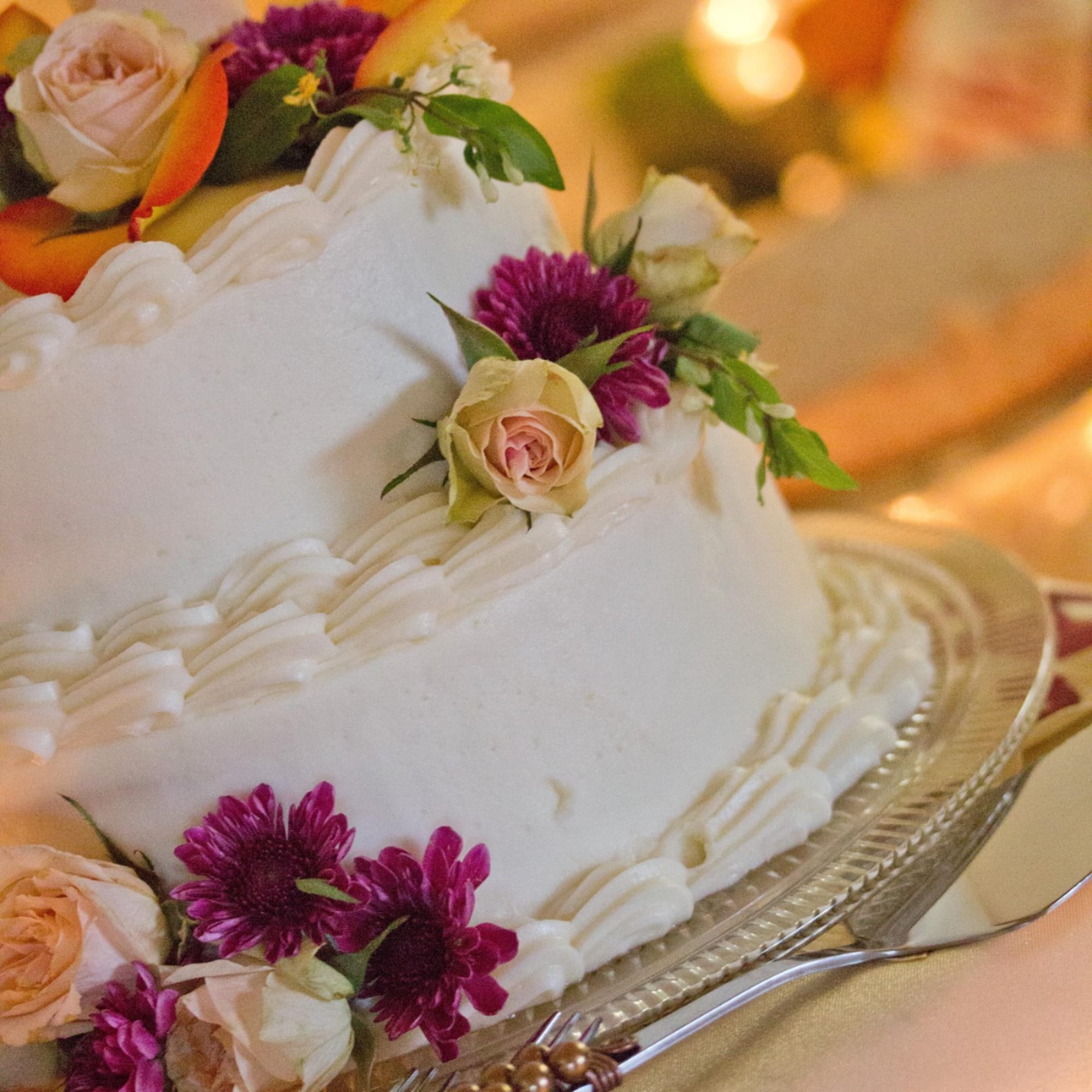 White tiered cake decorated with pale roses and purple flowers