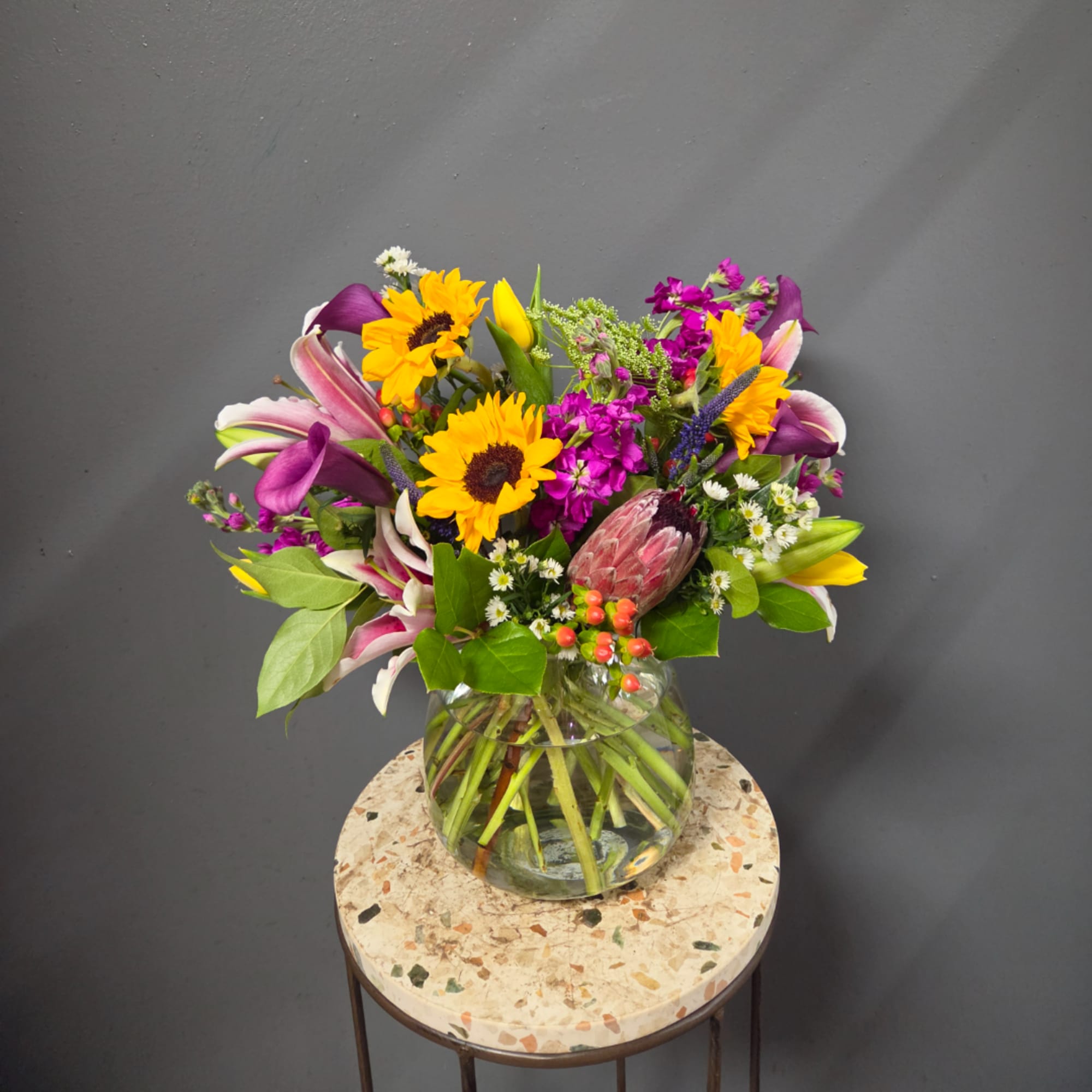 Mixed bouquet with sunflowers, lilies, and purple flowers in a glass vase