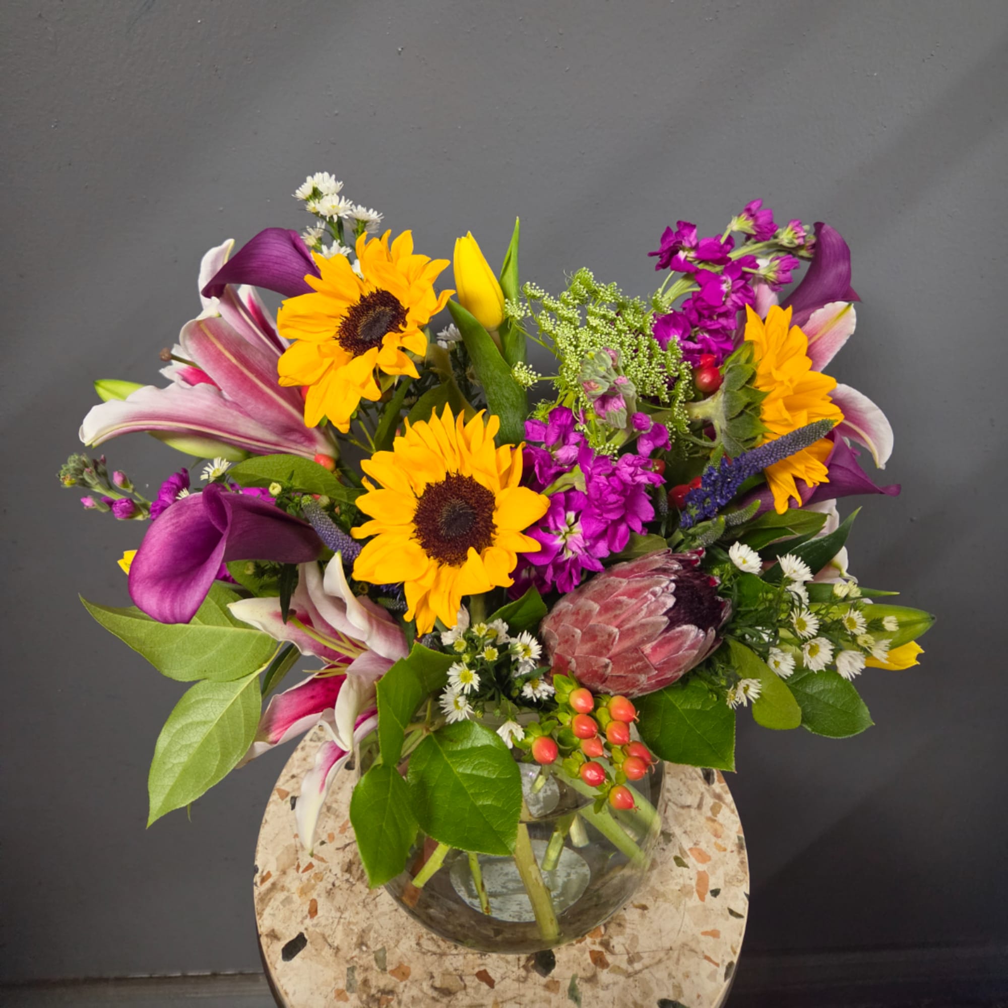 Mixed bouquet with sunflowers, lilies, purple calla lilies, and a glass vase