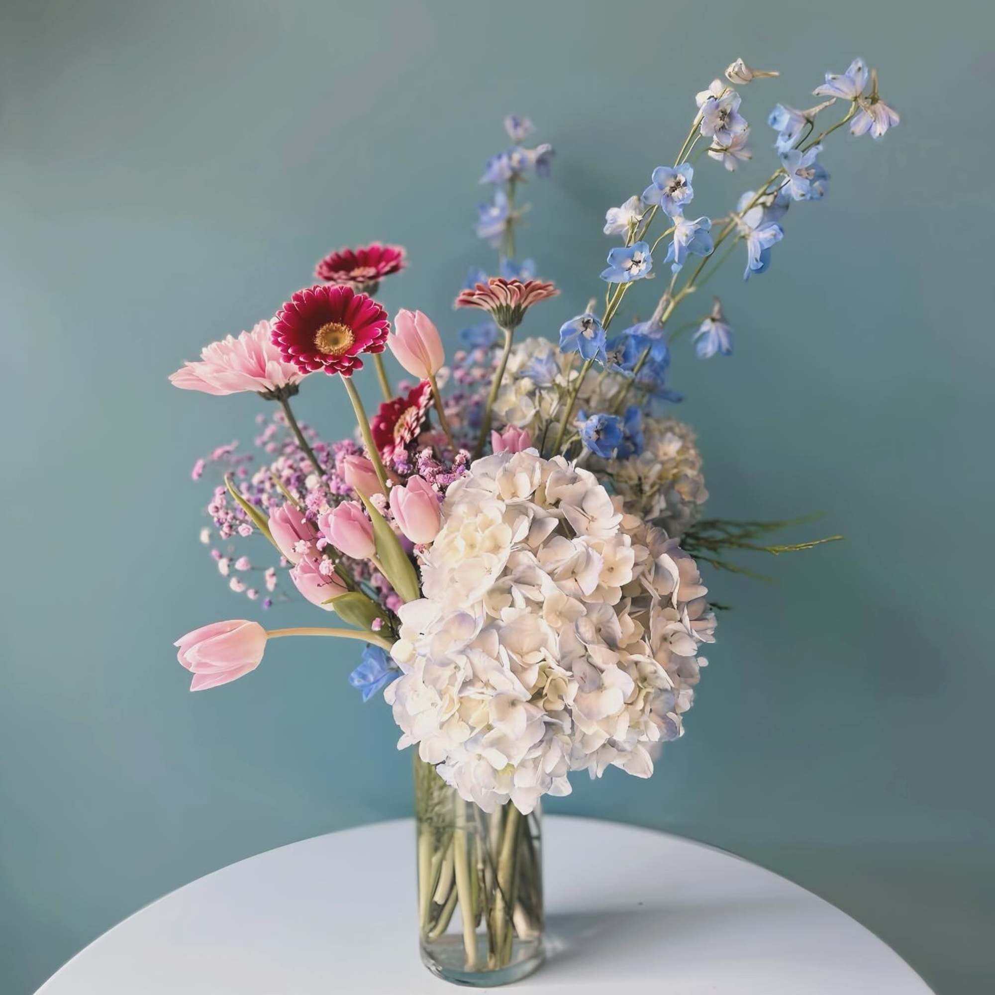 Mixed pastel bouquet in a clear glass vase with hydrangea, tulips, and daisies