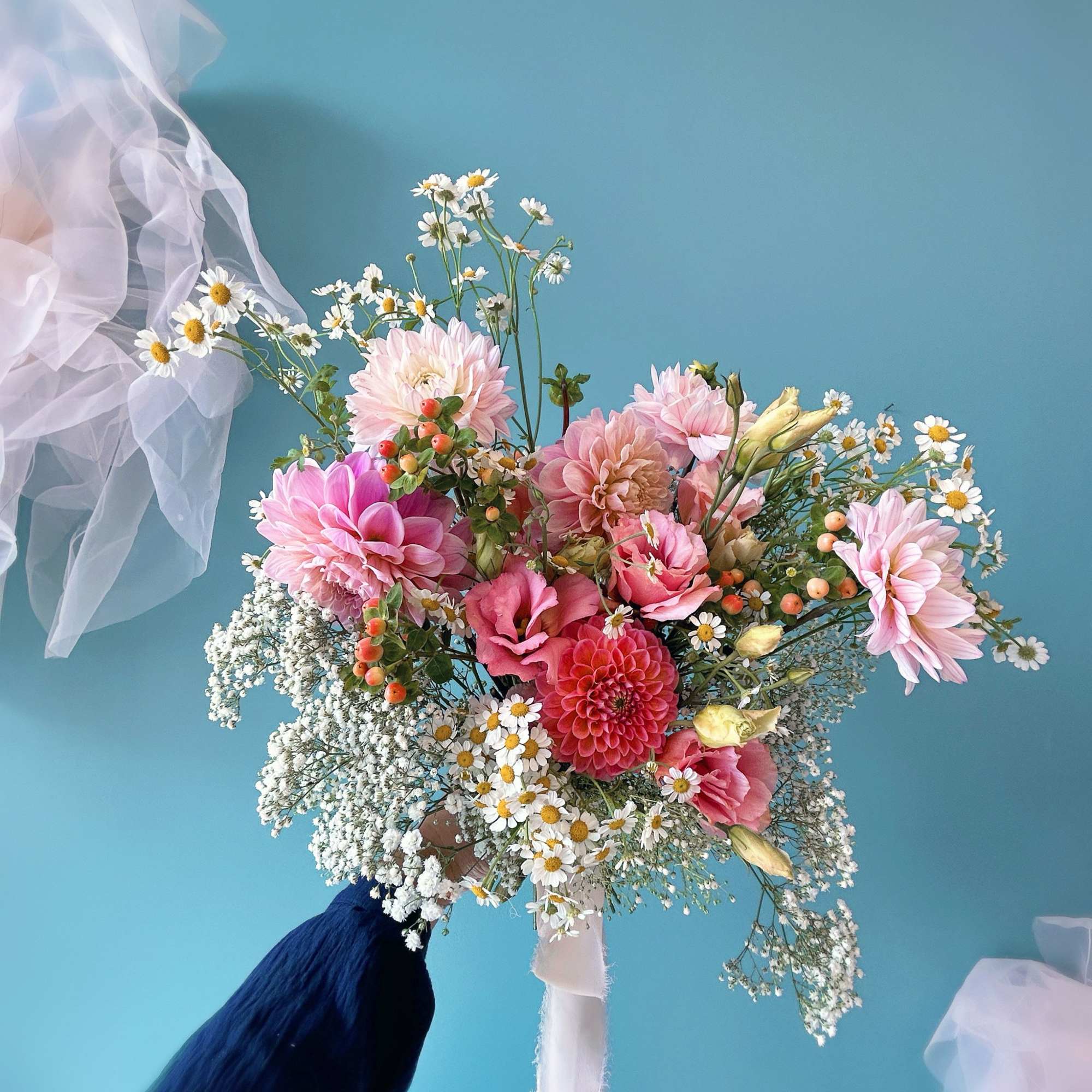 Hand-tied bouquet of pink blooms and small white daisies with a white ribbon