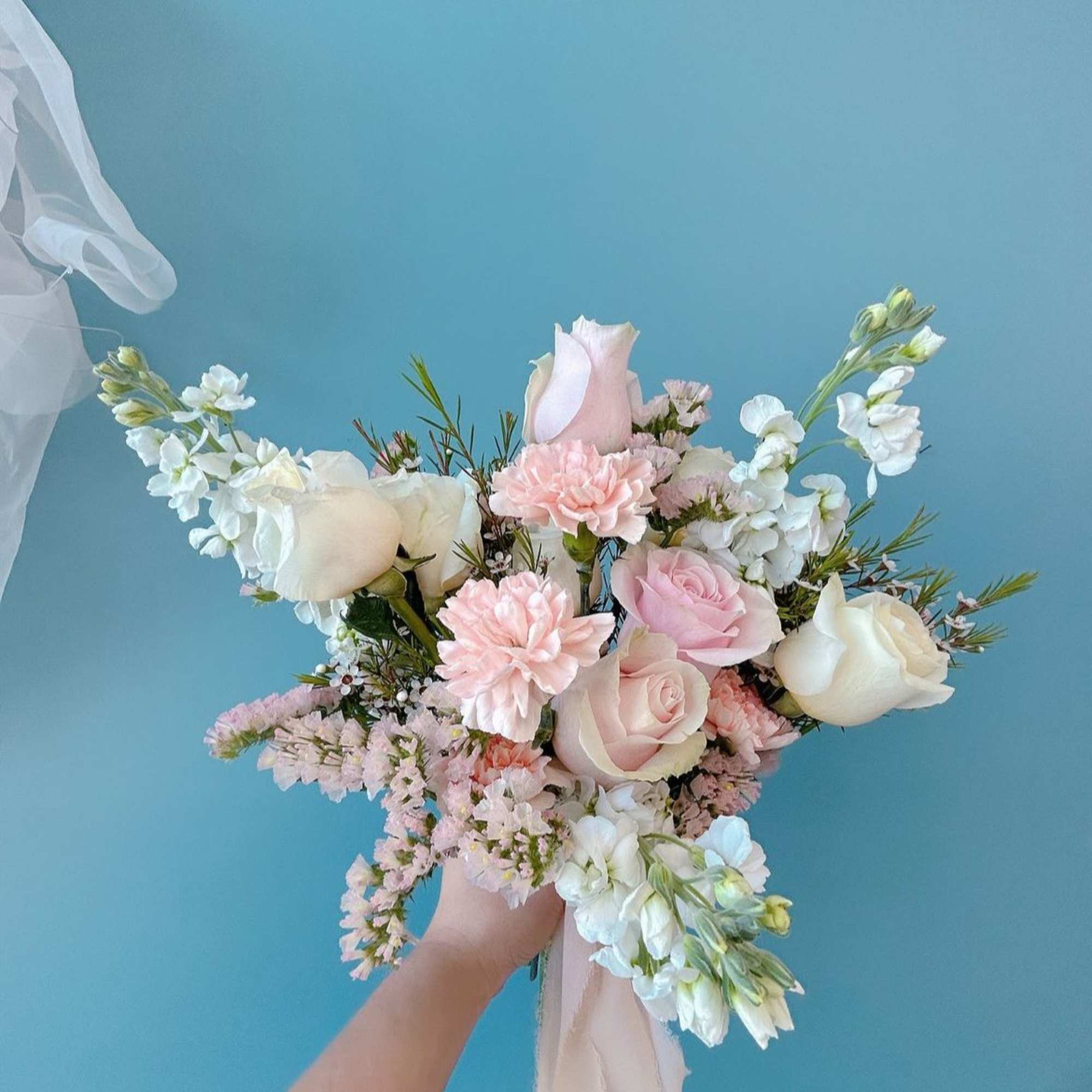 Handheld bouquet of pale pink and white roses with soft filler flowers