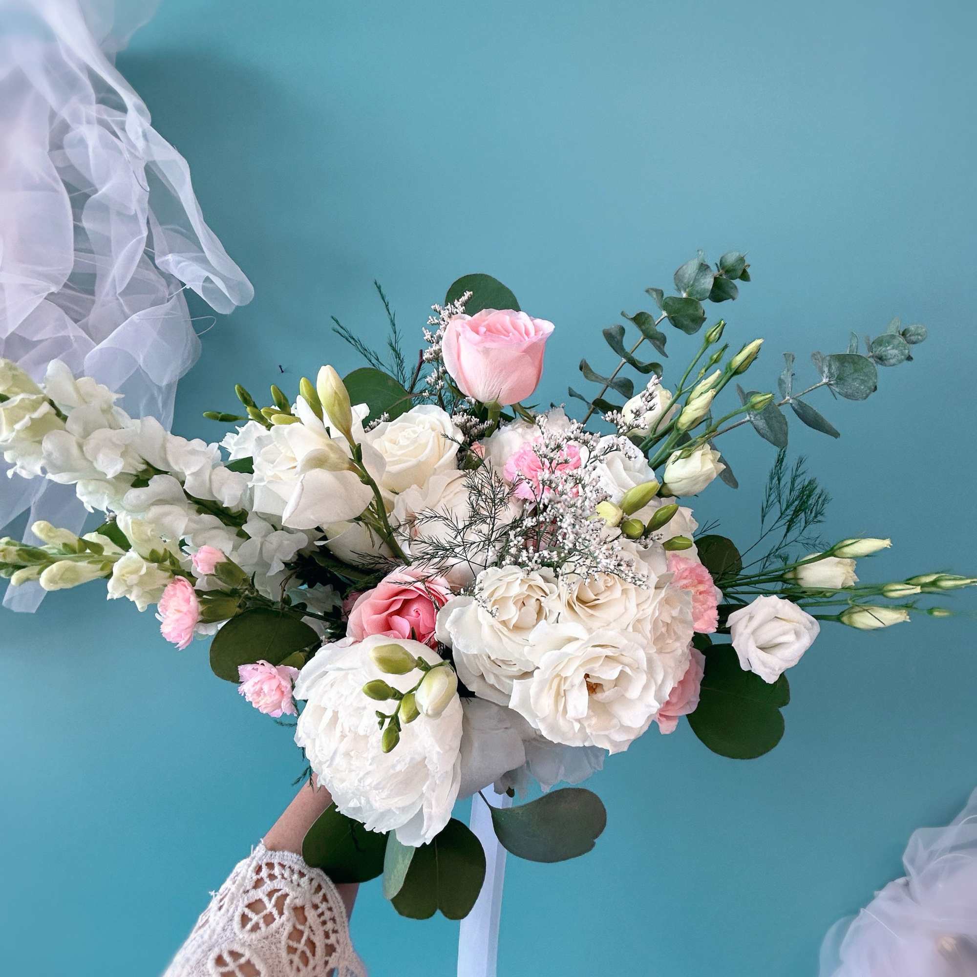 Handheld bridal bouquet of white and pink roses with airy greenery