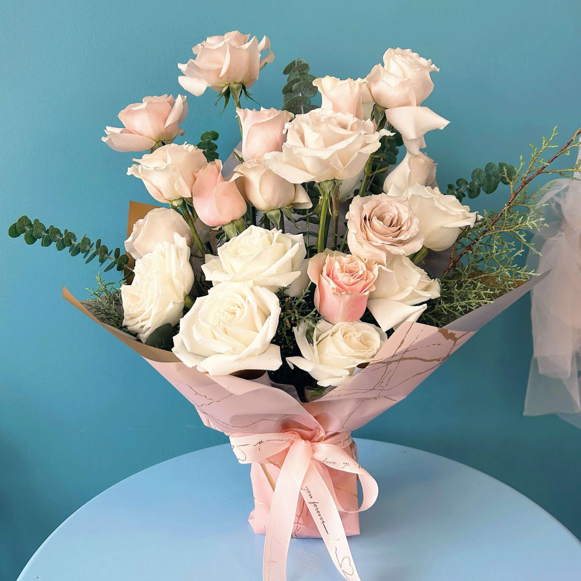 Bouquet of pale pink and white roses wrapped in pink paper with a ribbon