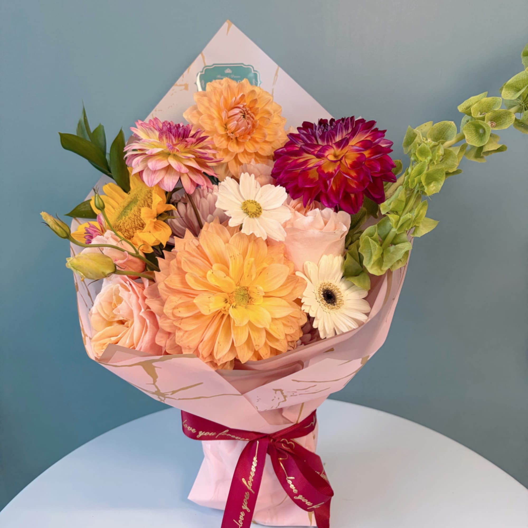 Colorful bouquet of dahlias and daisies wrapped in pink paper