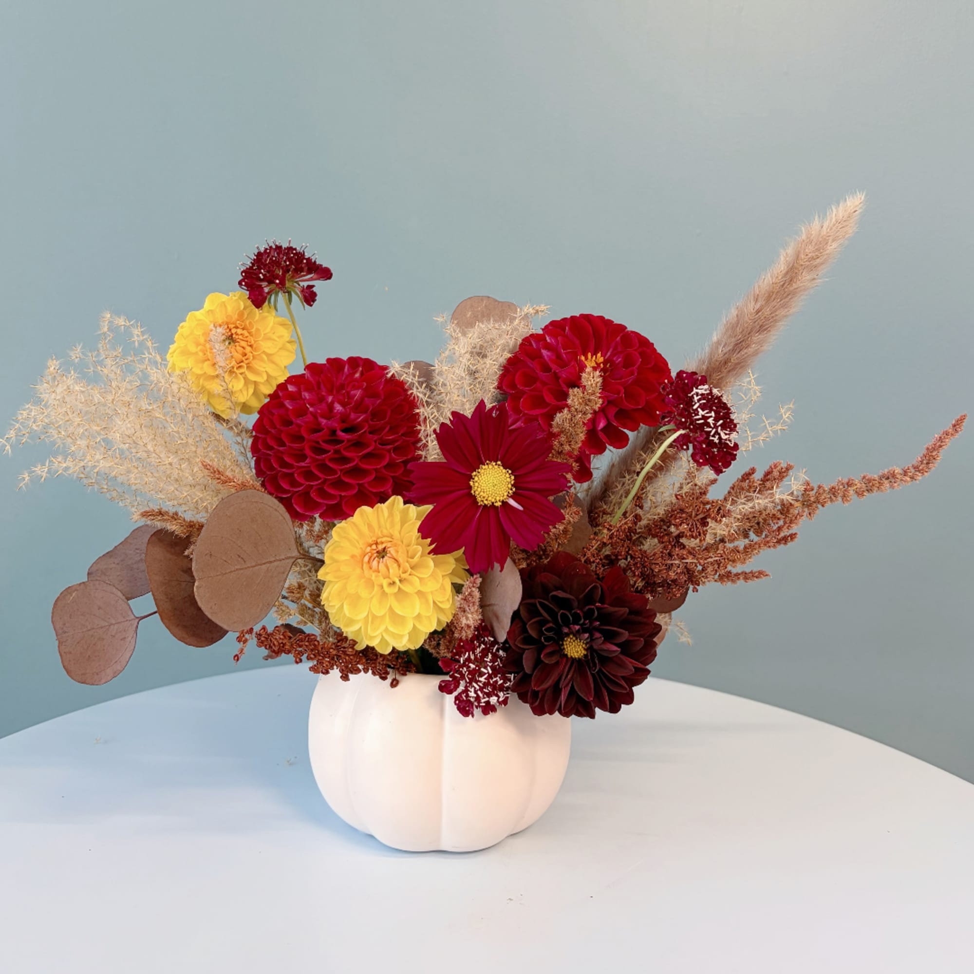 Mixed red and yellow flowers in a white pumpkin-shaped vase