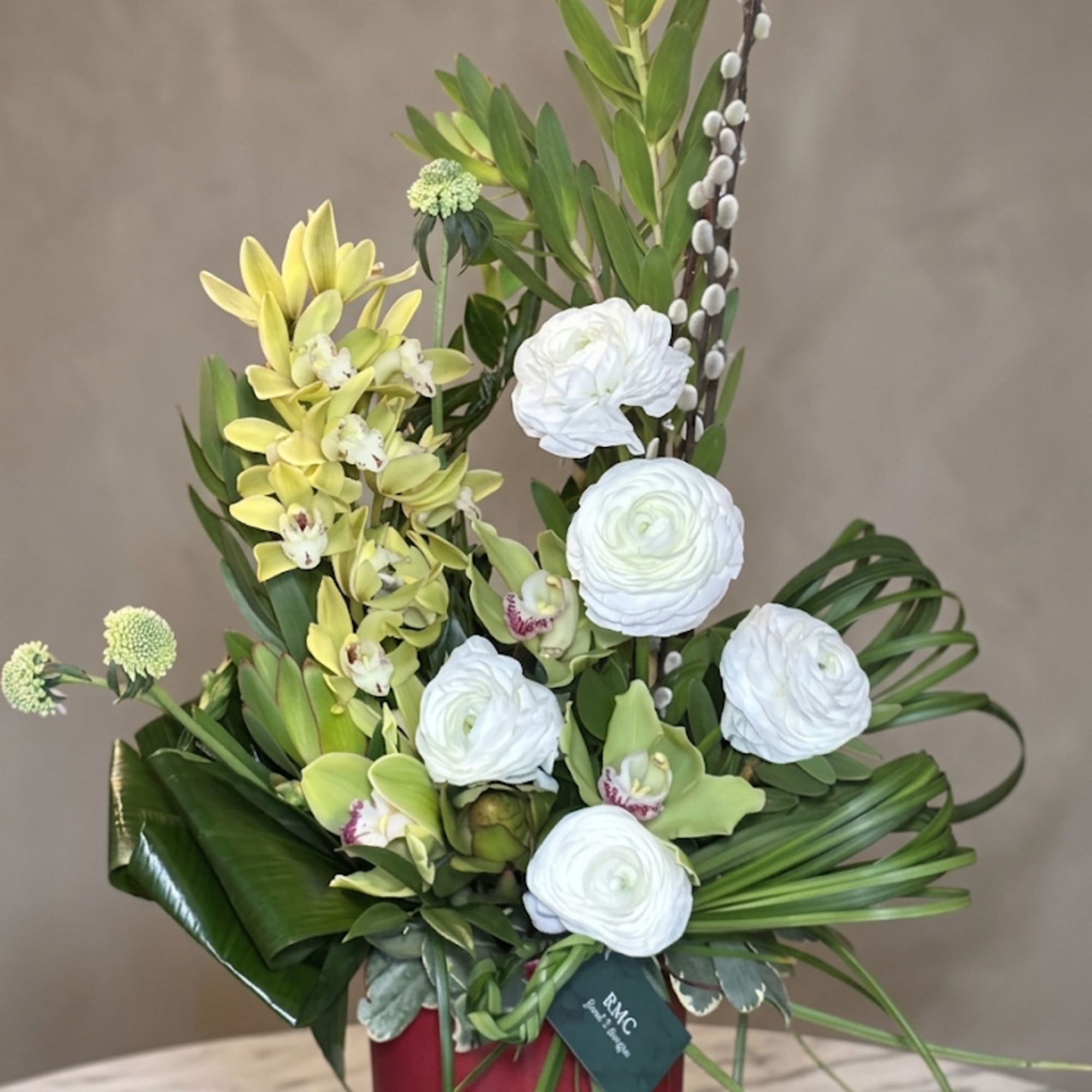Tall floral arrangement with white blooms and yellow orchids in a red vase