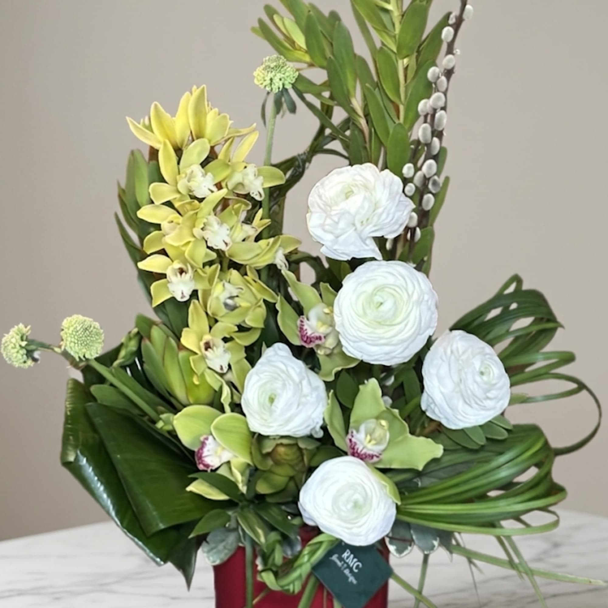 Green and white floral arrangement in a red container