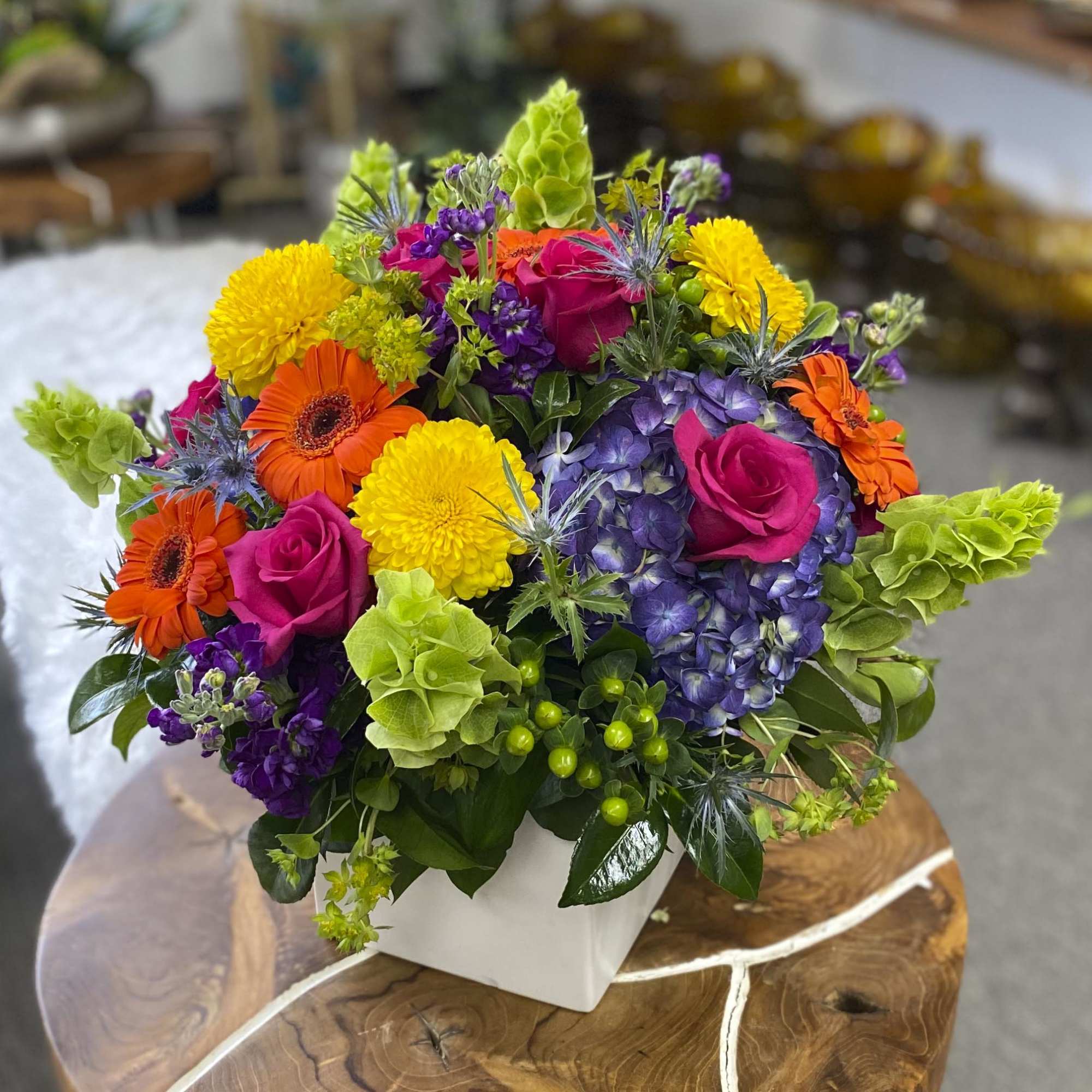 Colorful bouquet of roses, gerbera daisies, hydrangea, and mums in a white vase