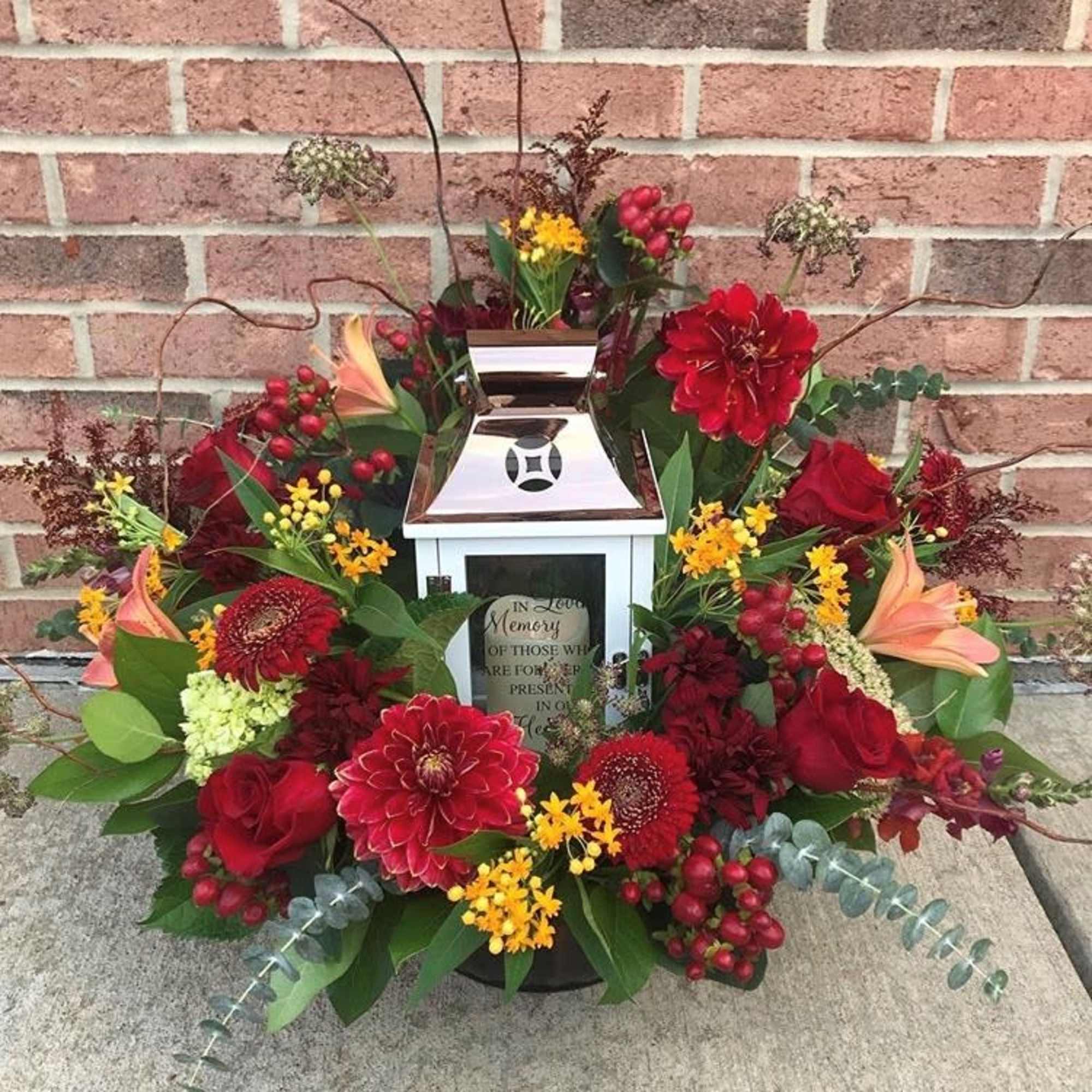 Sympathy floral arrangement around a white lantern with red and yellow flowers