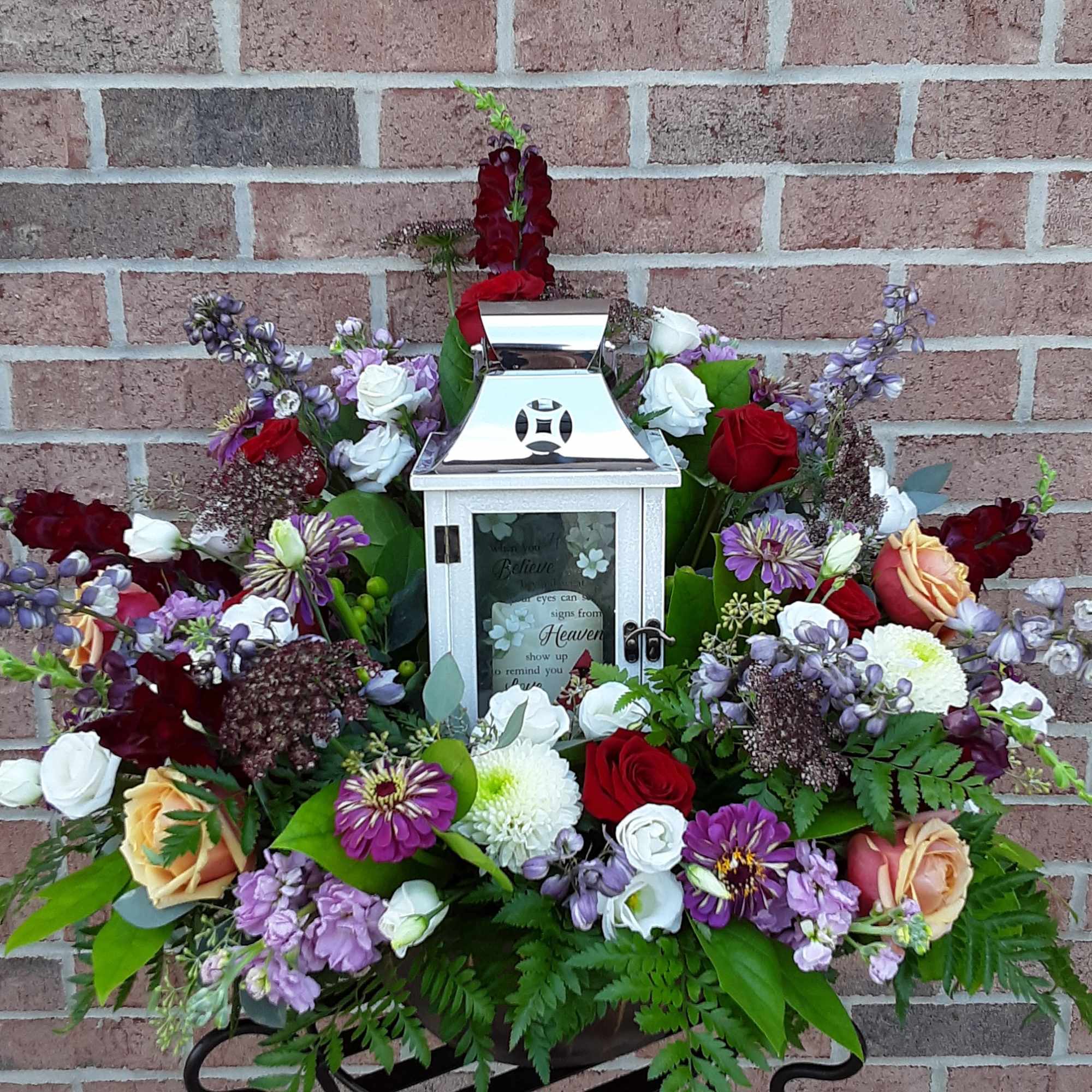 Floral arrangement around a silver lantern with red, white, purple, and peach flowers