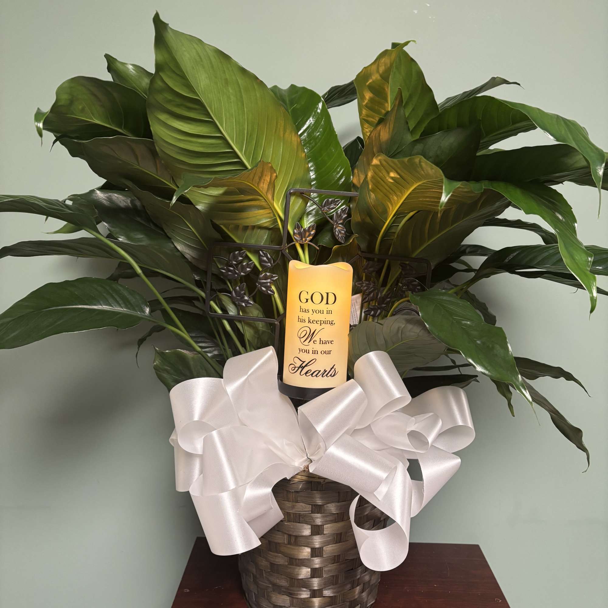 Potted green plant with a memorial candle and white ribbon in a woven basket