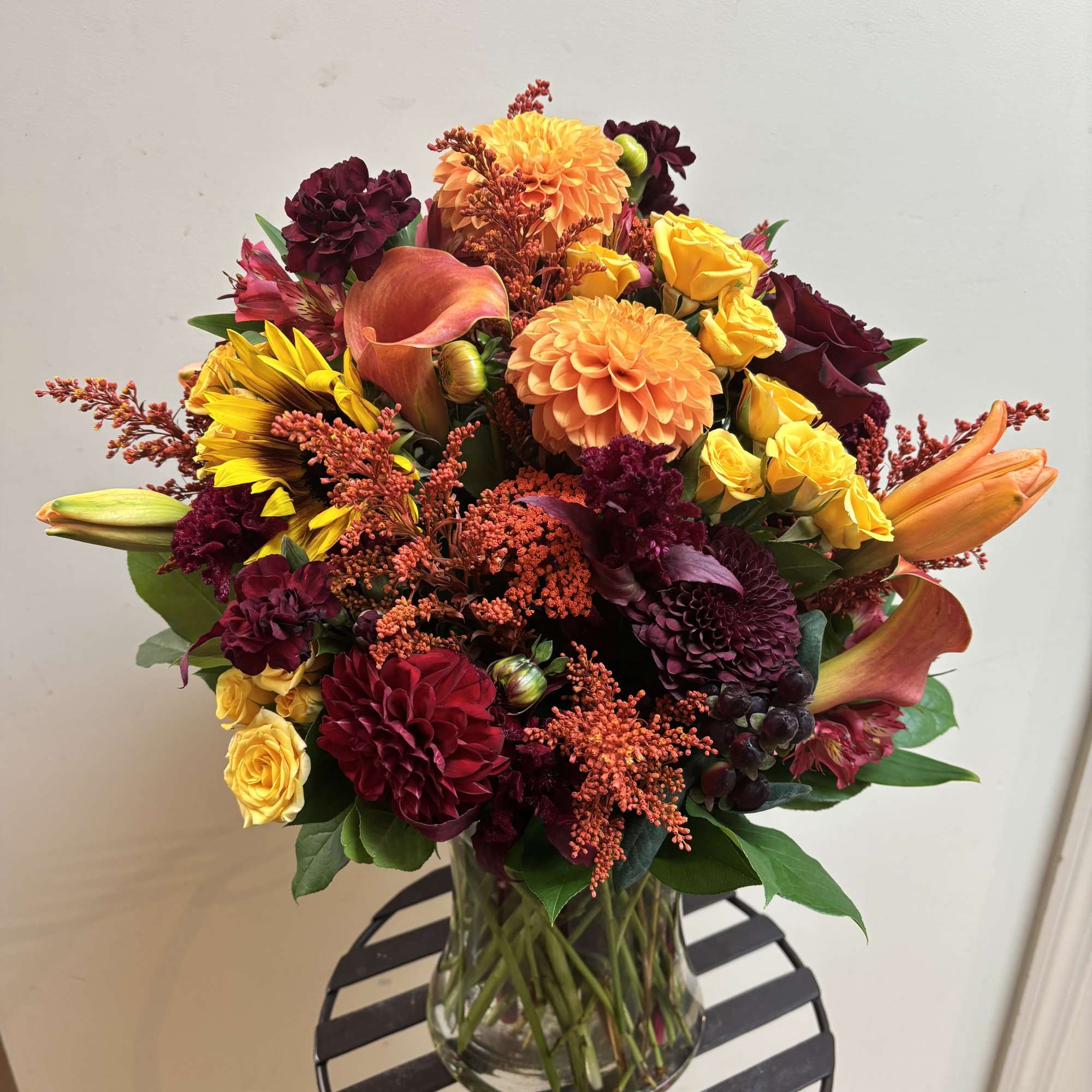 Bouquet of orange, yellow, and burgundy flowers in a clear glass vase
