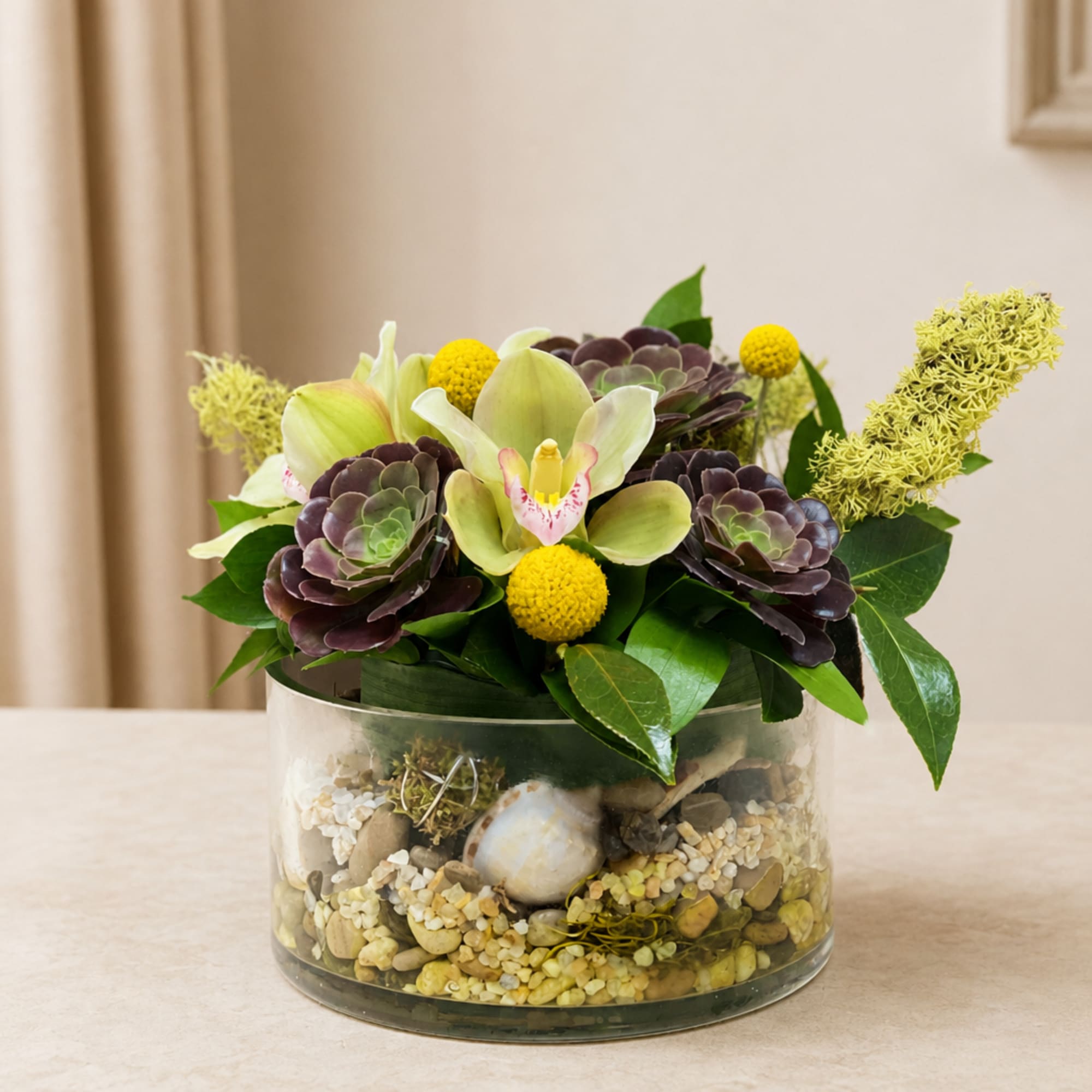 Succulent and orchid arrangement in a glass bowl with decorative stones