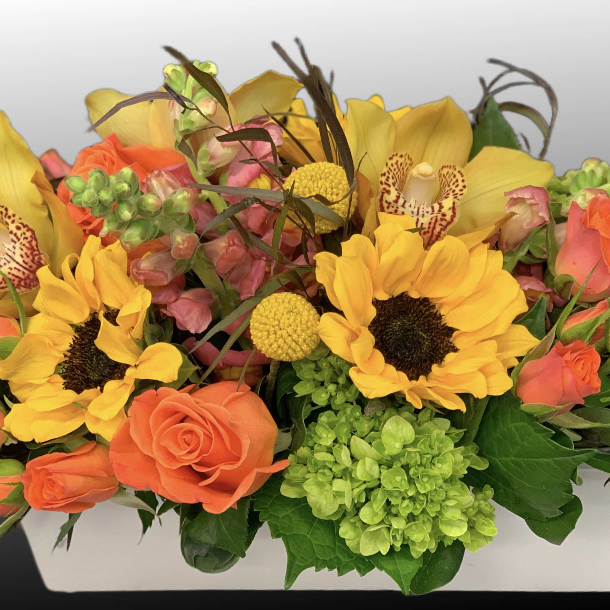 Bright bouquet of yellow sunflowers, orange roses, and orchids in a white box