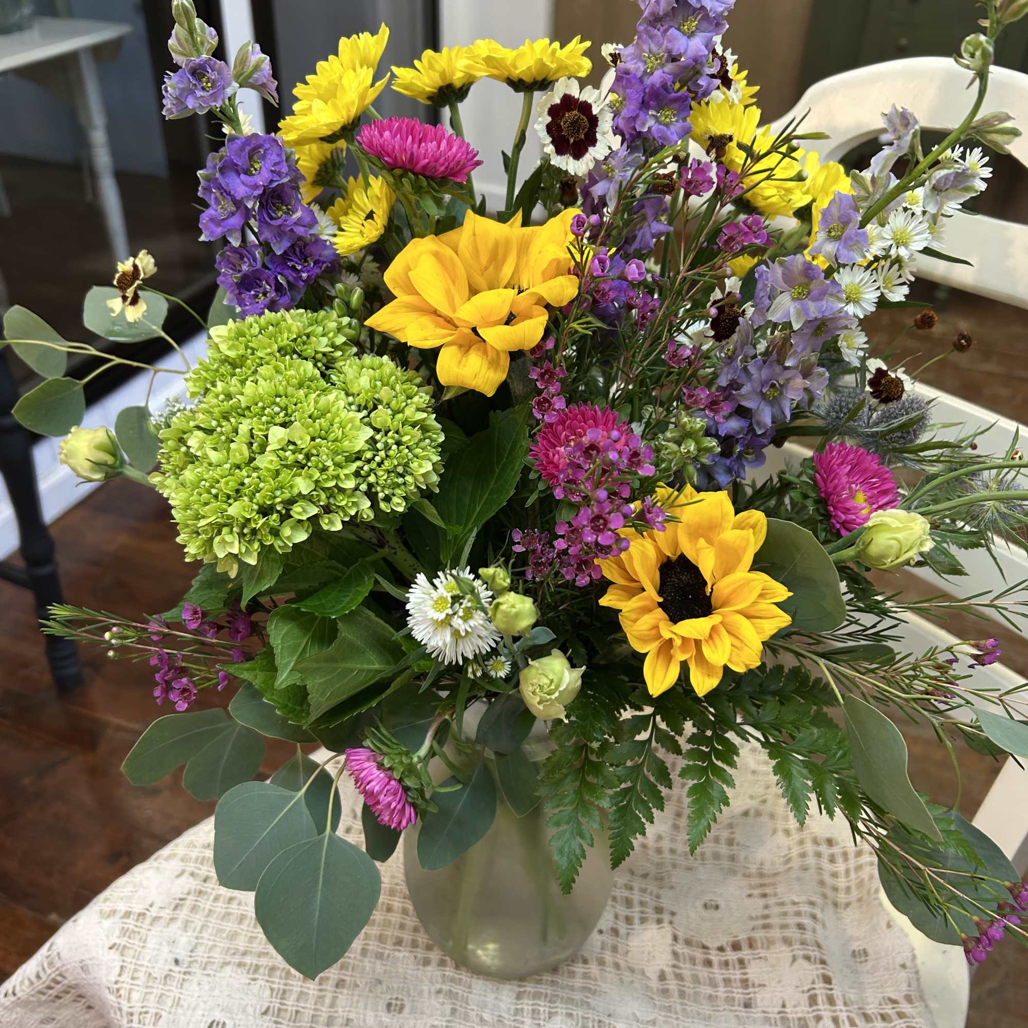 Mixed bouquet with yellow sunflowers, purple blooms, and green hydrangea in a glass vase