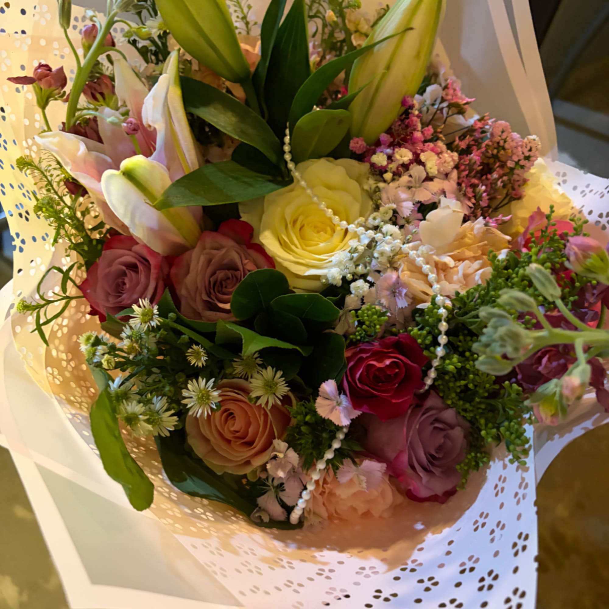 Mixed bouquet of roses, lilies, and small pink filler flowers wrapped in white paper