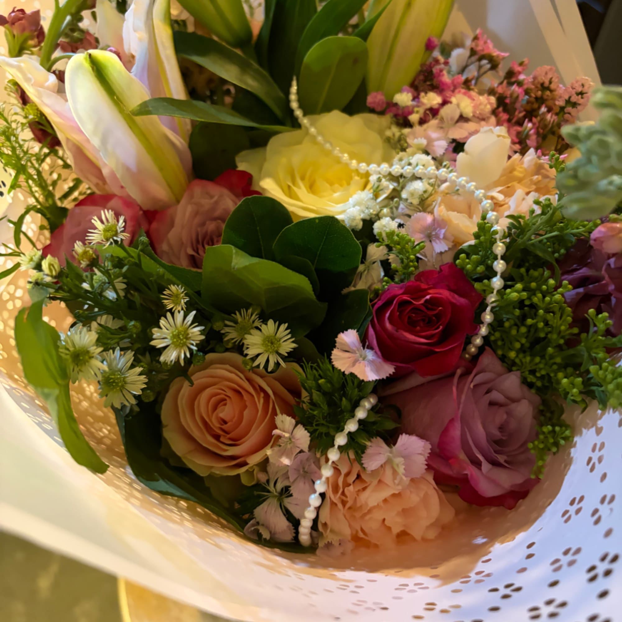 Mixed bouquet with roses, lilies, and small filler flowers wrapped in white paper