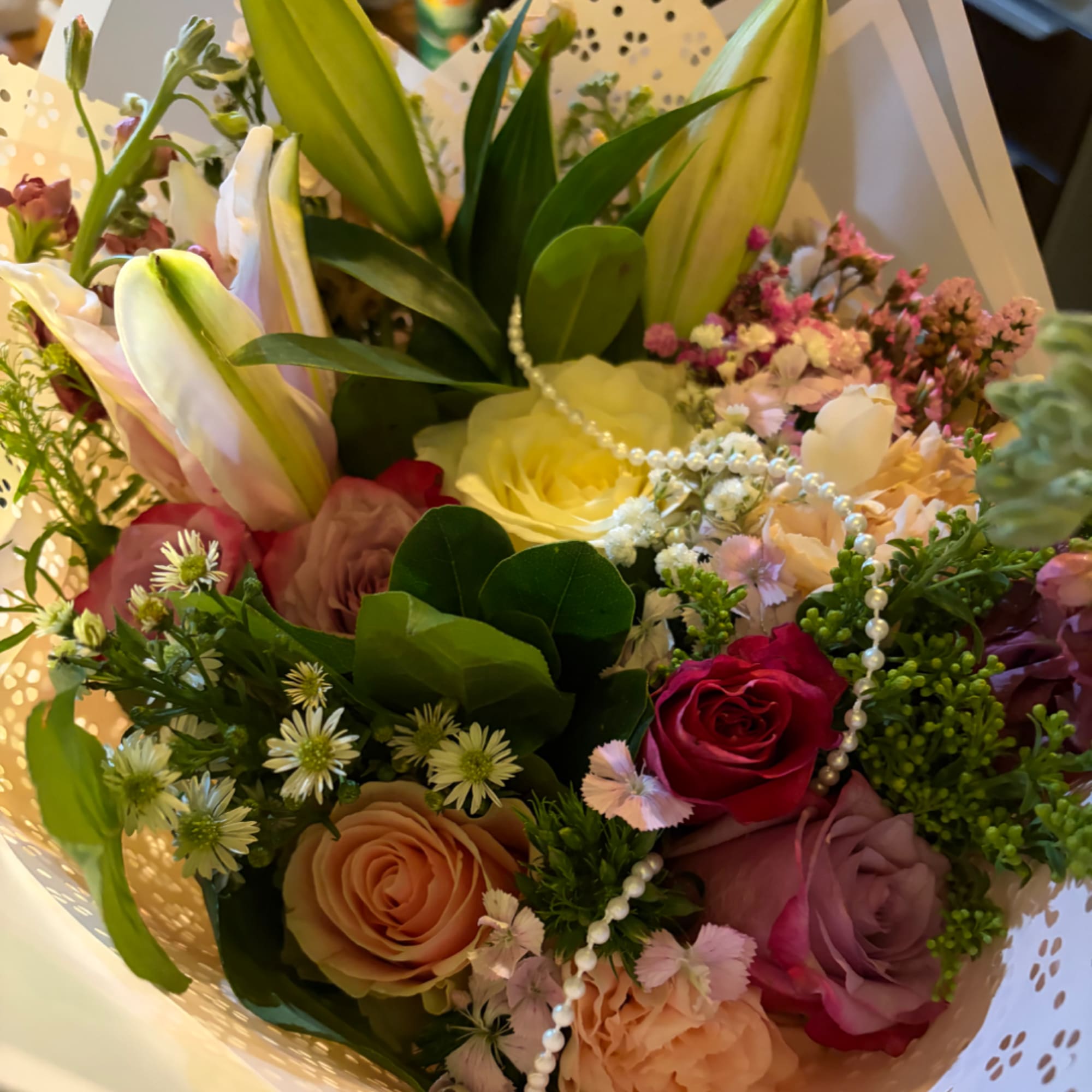 Mixed bouquet of roses and lilies with pearl strands in decorative wrap