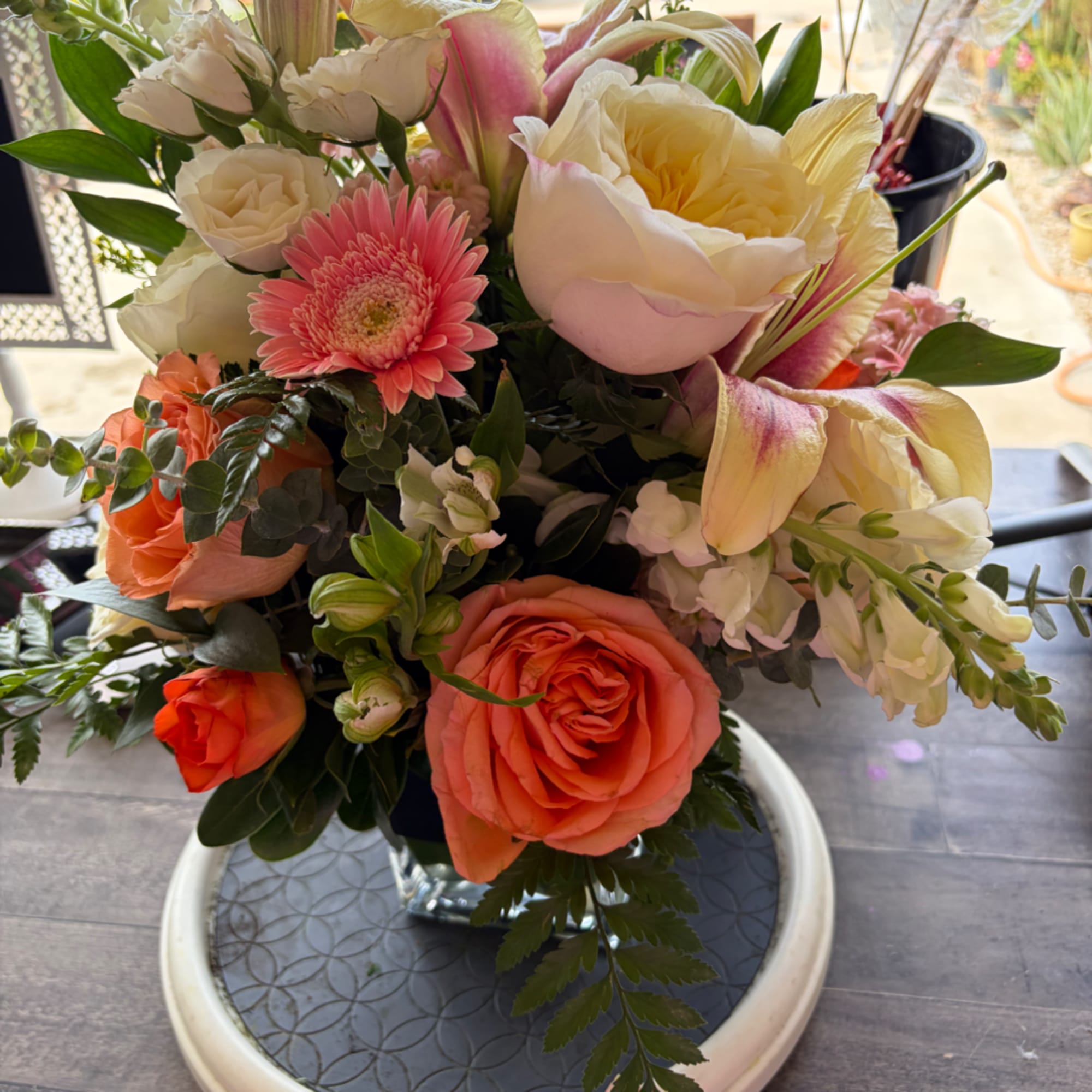 Mixed bouquet with peach roses, pink gerbera daisies, and white lilies in a glass vase