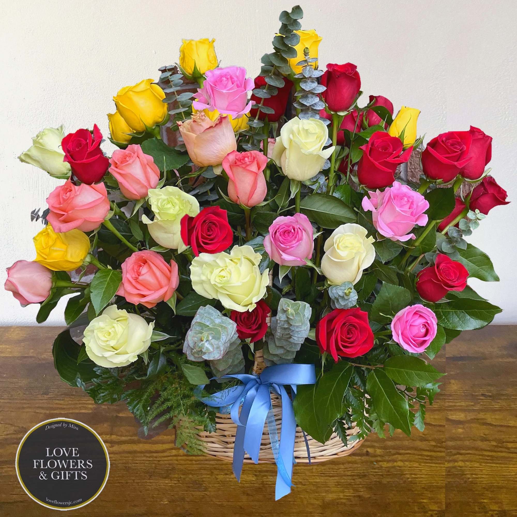 Large basket of mixed-color roses with a blue ribbon bow at the front.
